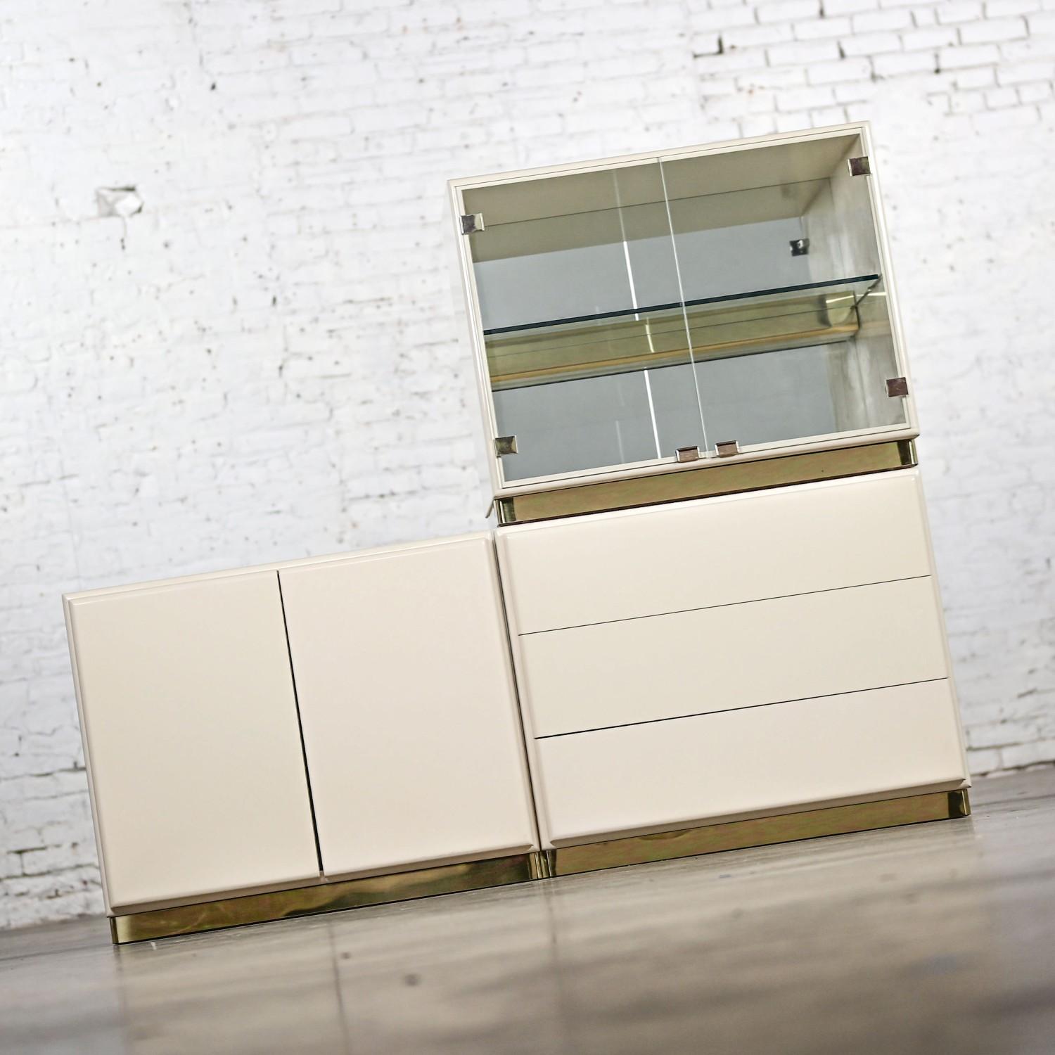 Impressive 1980’s Modern Less Is More II Collection modular casegood storage system by Milo Baughman for Thayer Coggin comprised of 3 off white lacquered cabinets including 1 lighted glass unit w/a single adjustable glass shelf & brass light bar, a