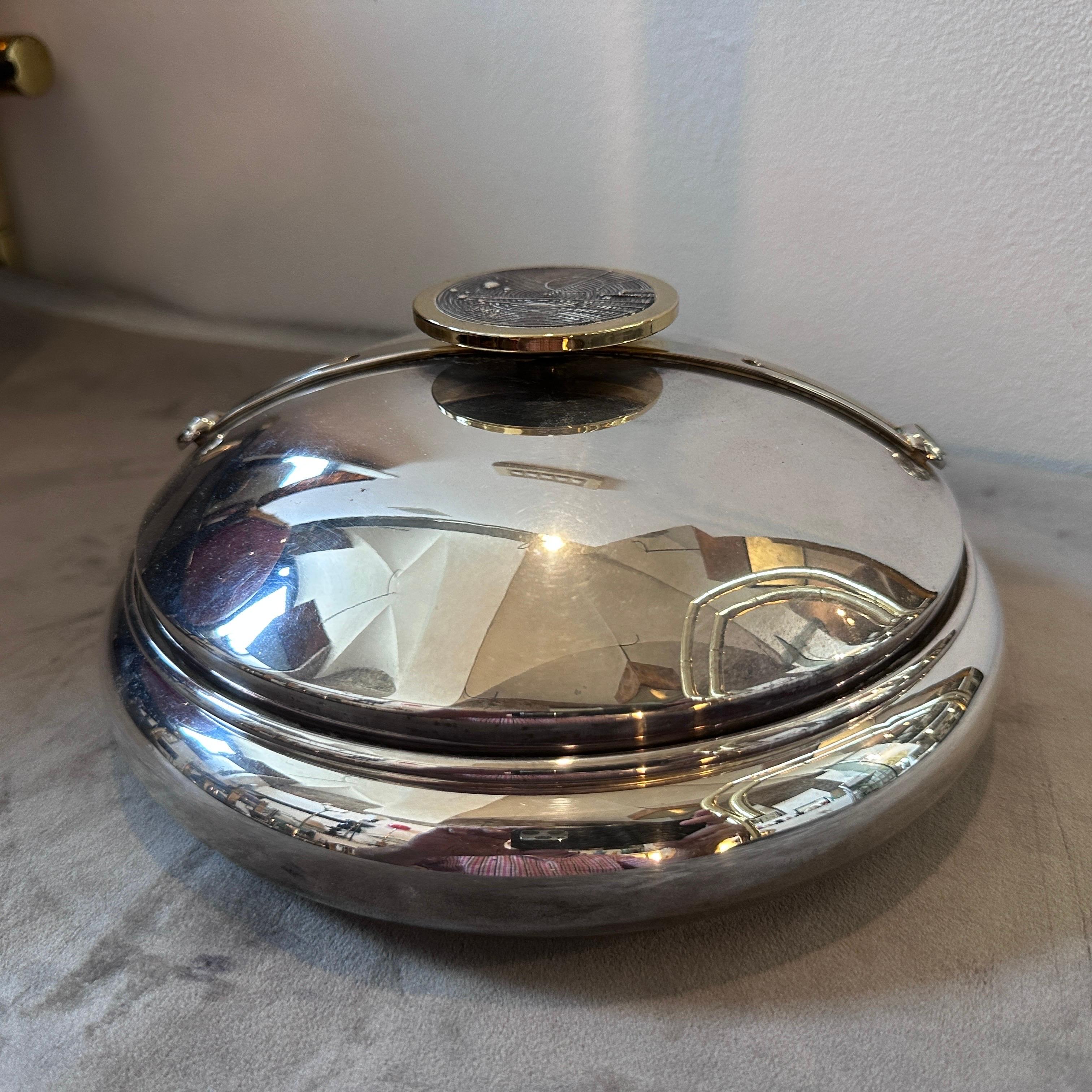 Une boîte ronde en métal argenté et en laiton, conçue et fabriquée en Italie dans les années quatre-vingt. Il est en très bon état, sur le couvercle, à l'intérieur d'un cadre en laiton, il y a un décor abstrait en métal. Il s'agit d'une pièce de