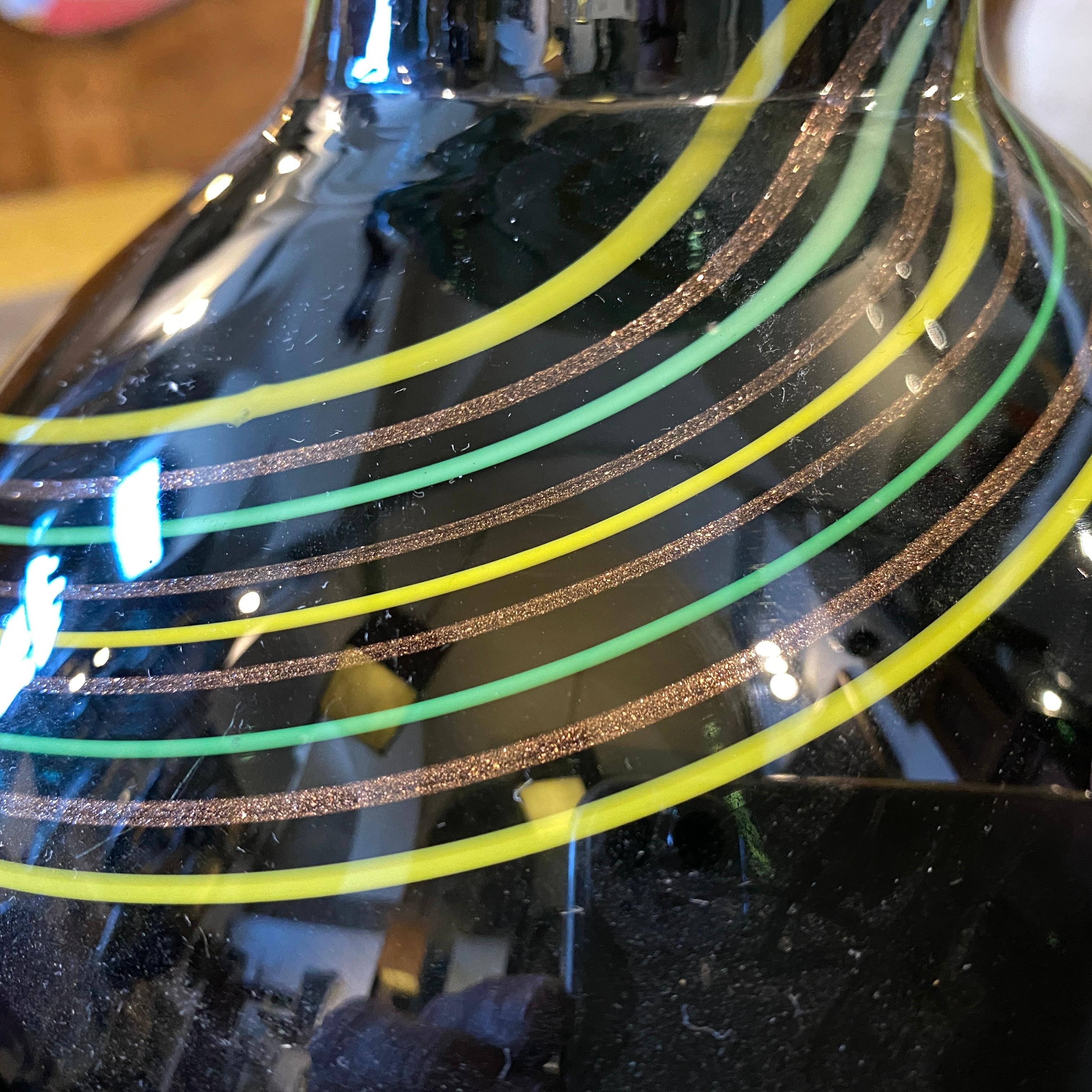 Un vase en verre de Murano noir décoré de rayures vertes, brunes et jaunes. Il est en très bonnes conditions, signé sur le fond style murano.
