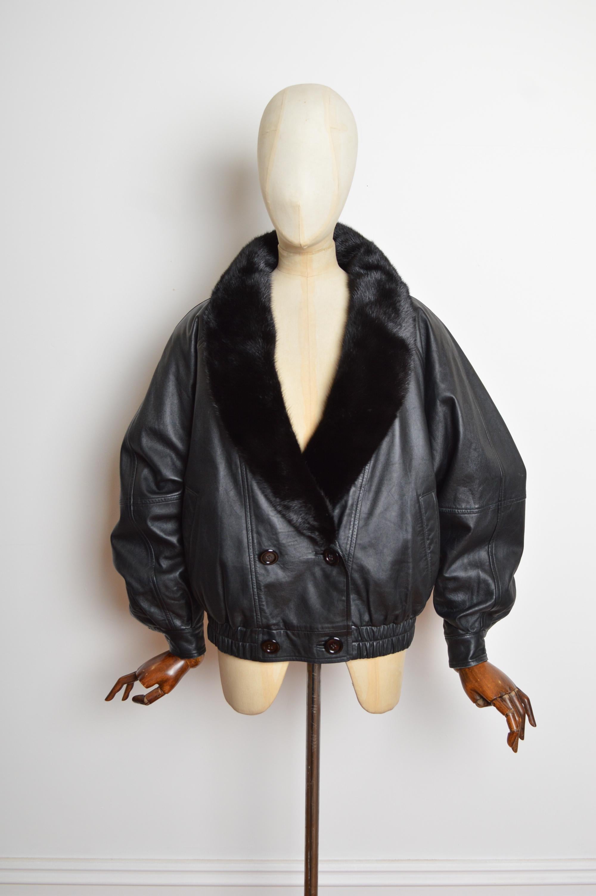 Giacca chic anni '80 in pelle nera con colletto staccabile in pelliccia di visone lucida e felpata, con maniche lunghe, bottoni sul davanti e tasche sui fianchi foderate in velluto.
La giacca è foderata con un tipico jacquard iridescente stile anni