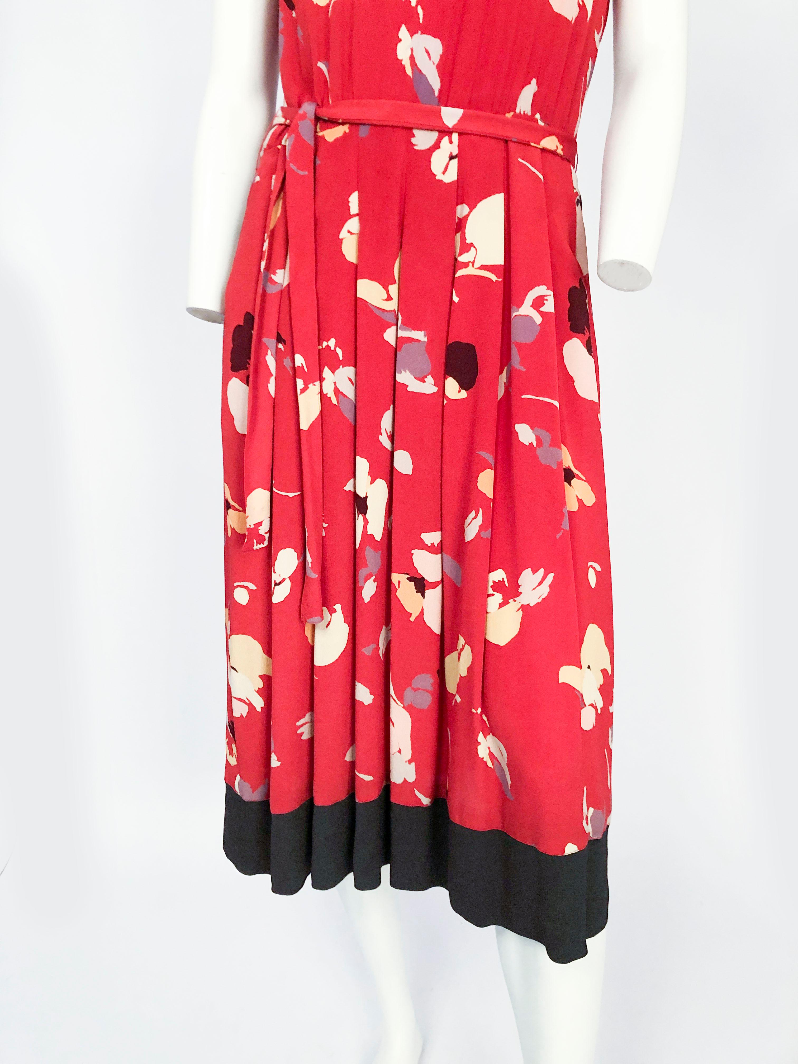 robe imprimée rouge Nipon des années 1980 avec motif impressionniste, encolure bateau modifiée, bordure noire sur les manches, l'encolure et l'ourlet. Ceinture assortie, plis au couteau sur la jupe et fermeture à glissière/bouton au dos de la robe.