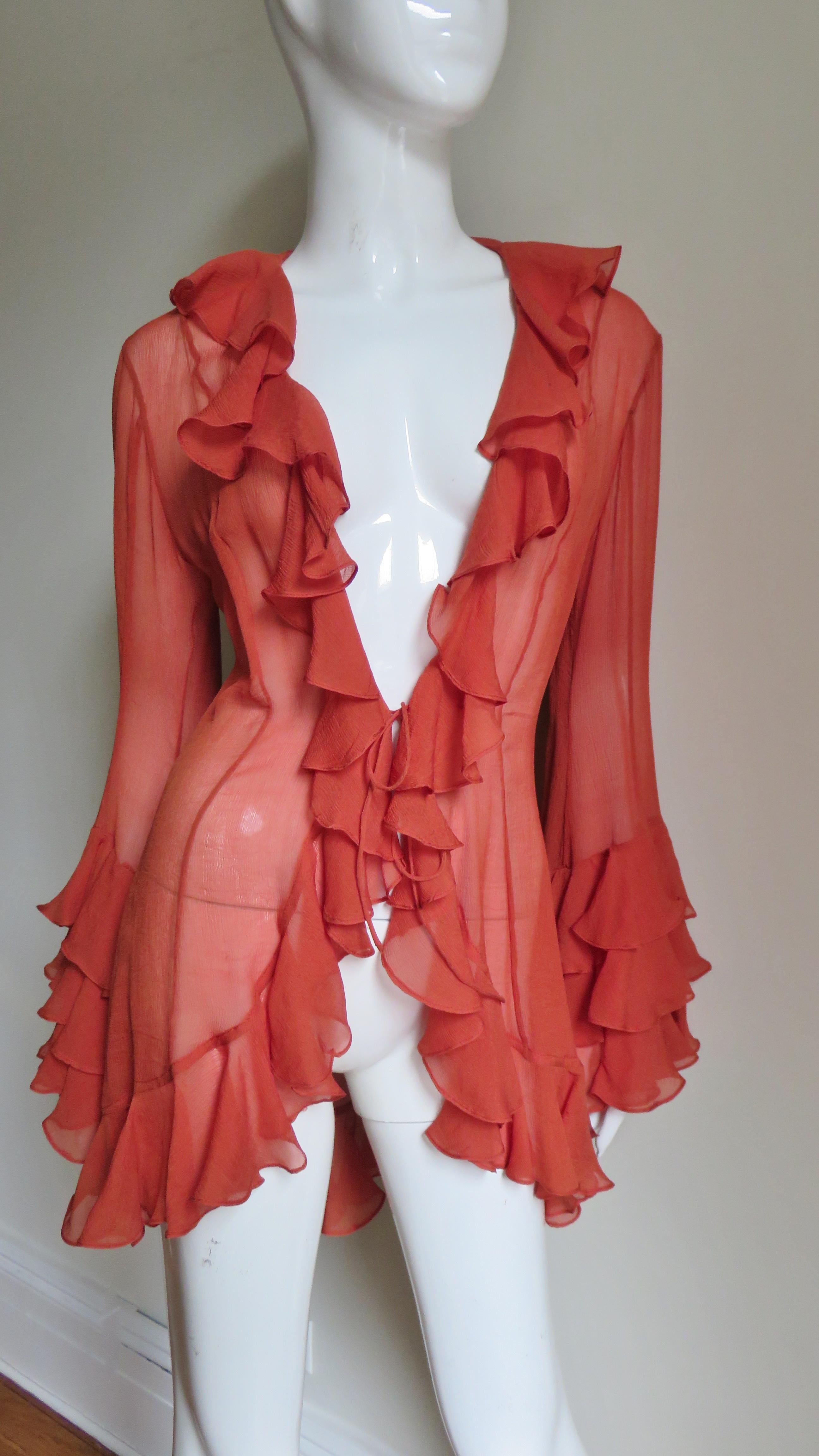 A fabulous orange silk top, shirt, blouse from Norma Kamali.  It has a ruffle around the neckline, front, and hemline plus 3 rows of them around the bottom of the bell sleeves.  It has princess seaming for a great fit, ties at the waist and it