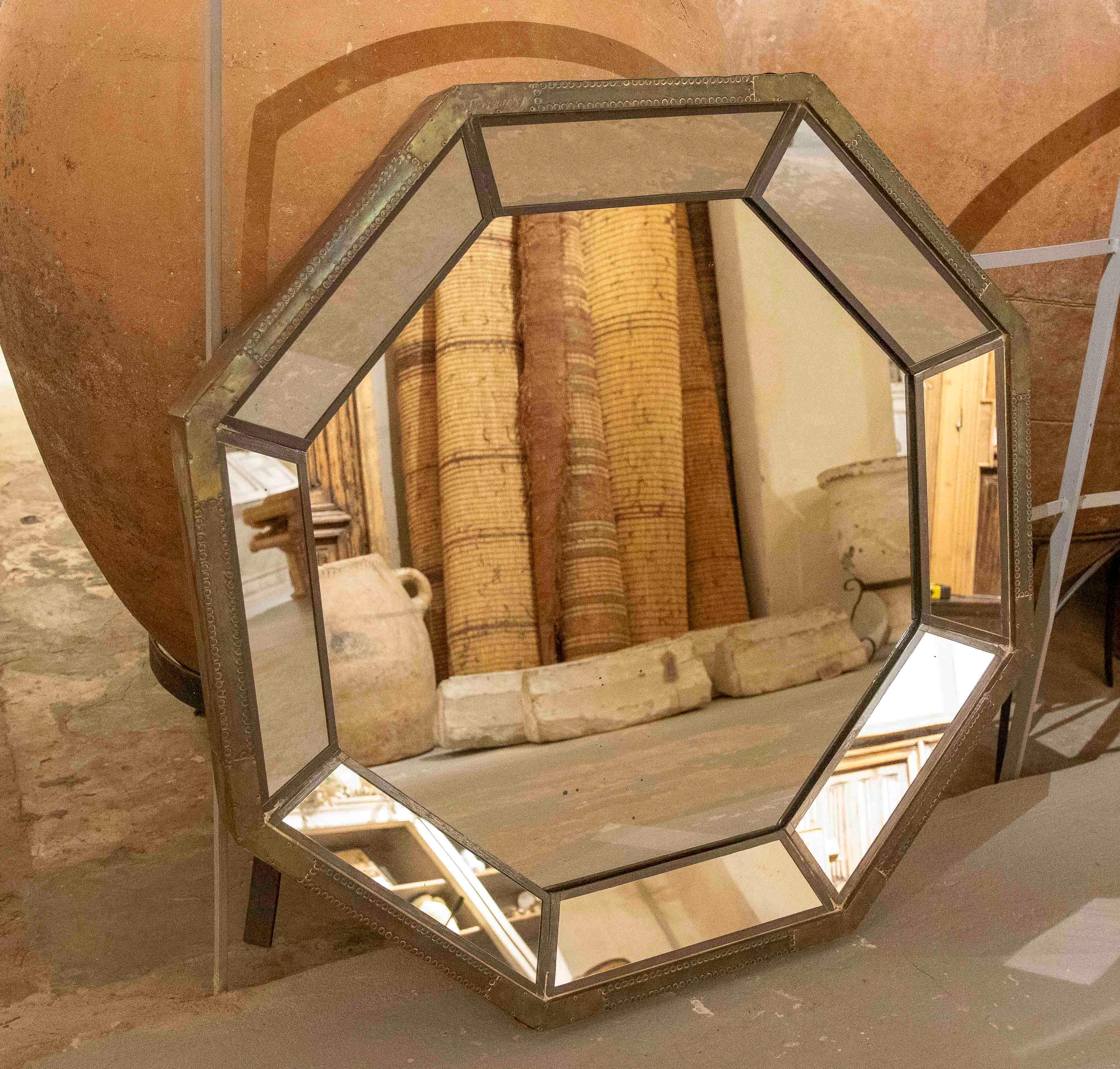 Un élégant miroir octogonal avec un cadre en métal vieilli et des sections biseautées qui reflètent la lumière de manière subtile et sophistiquée. Sa structure géométrique et sa finition patinée ajoutent du caractère et de la profondeur, combinant