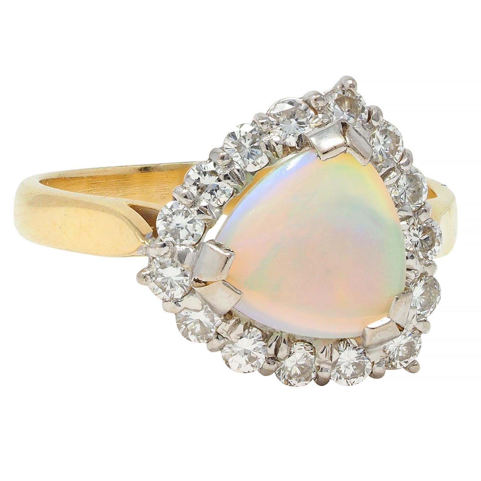 Centering a triangle-shaped opal cabochon measuring 8.0 x 8.0 mm 
Translucent white in body color with spectral play-of-color
Prong set in white gold head with halo surround 
Comprised of prong set round brilliant cut diamonds
Weighing approximately