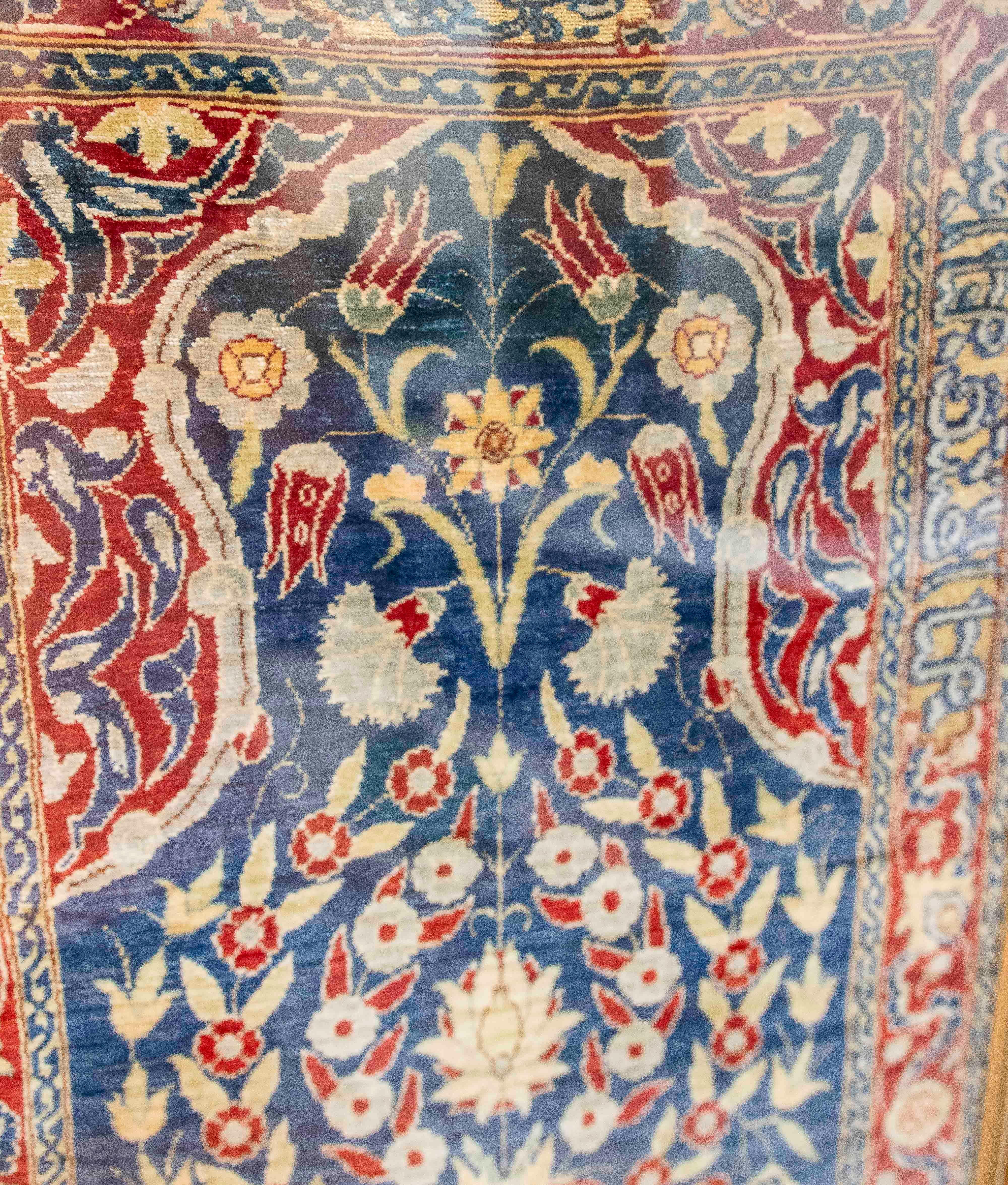Questo squisito arazzo ricamato a mano presenta un disegno simmetrico di ispirazione orientale incentrato su un vaso da cui spuntano fiori stilizzati, circondato da un'armoniosa composizione di motivi floreali, uccelli ed elementi decorativi.