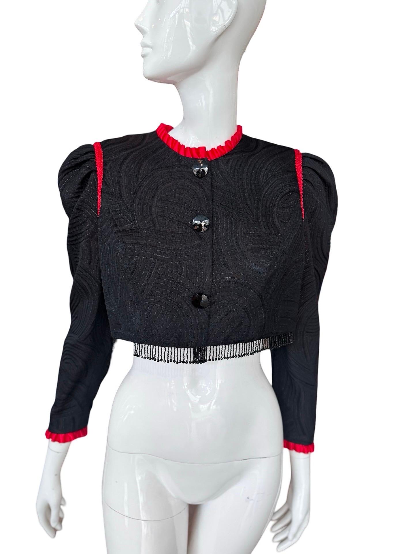 Splendido e scenografico bolero Oscar De La Renta in tessuto broccato nero con un filo scintillante dal design a volute. Il look è vivace grazie alle rifiniture rosse e ai volant intorno al colletto e ai polsini.  Ha una leggera manica a sbuffo e