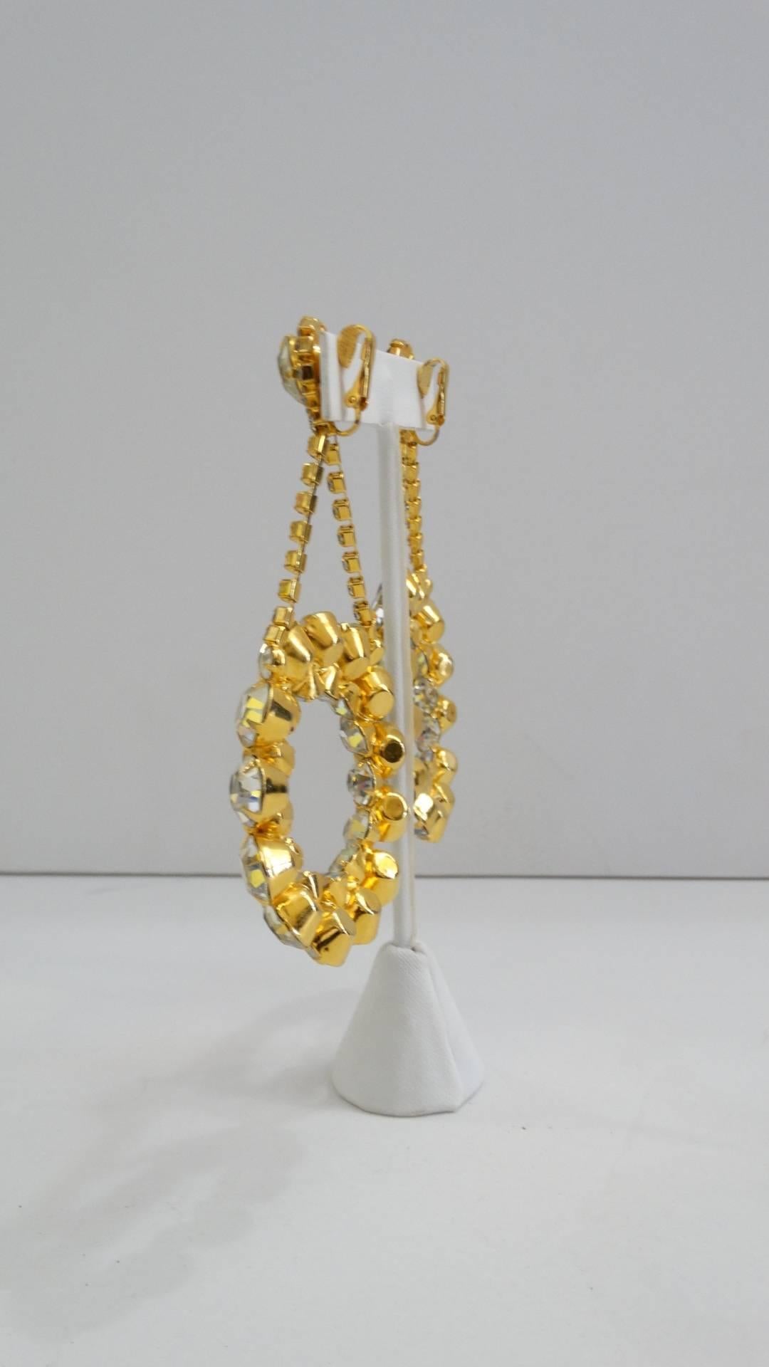 We love to rock a statement earring- and you will too with our oversized 1980s rhinestone hoop earrings! Made of a brilliant gold metal, encrusted with crystalline rhinestones. Drop style earring, with large hoop charms suspended from rhinestone