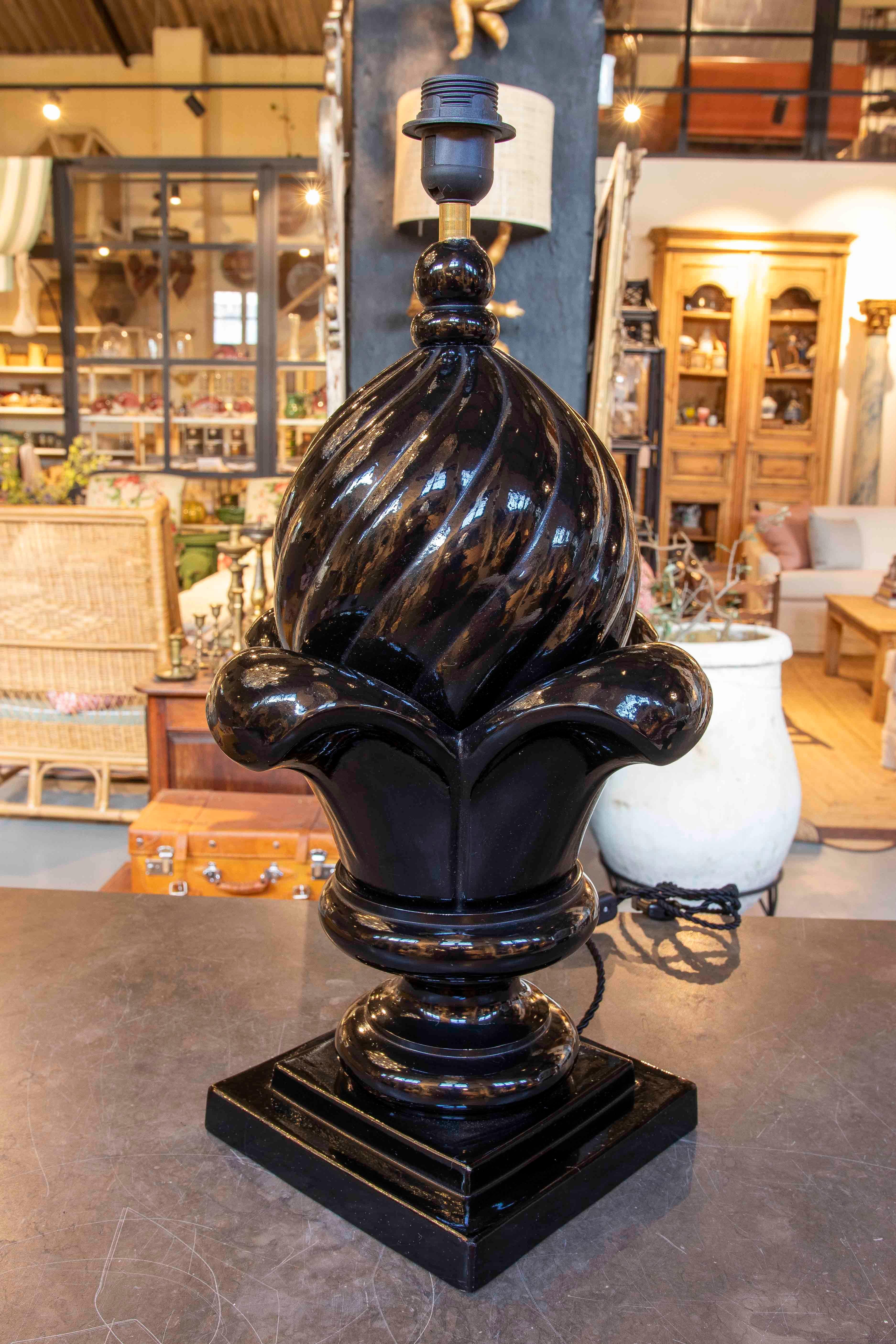 Pair of decorative lamps made of glossy black glazed ceramic. Its unique design features a stylized floral shape that combines soft curves and geometric details, evoking a classic and sophisticated aesthetic. Mounted on a square base, this piece is