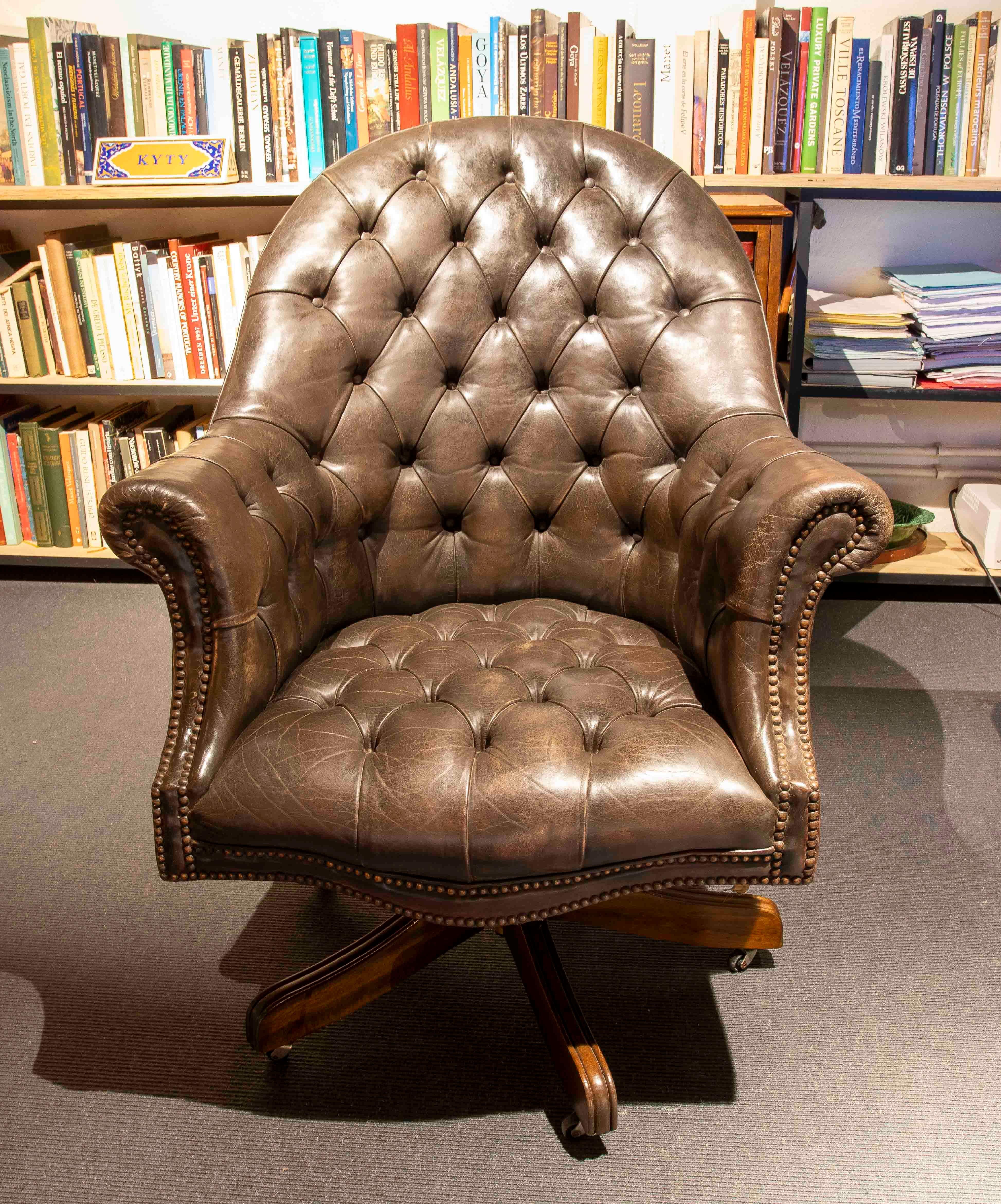 Elegante coppia di poltrone girevoli in stile Chesterfield, rivestite in pelle marrone di alta qualità con design capitonné che ne evidenzia il carattere classico e senza tempo. Ogni poltrona presenta braccioli curvi, schienale alto e dettagli