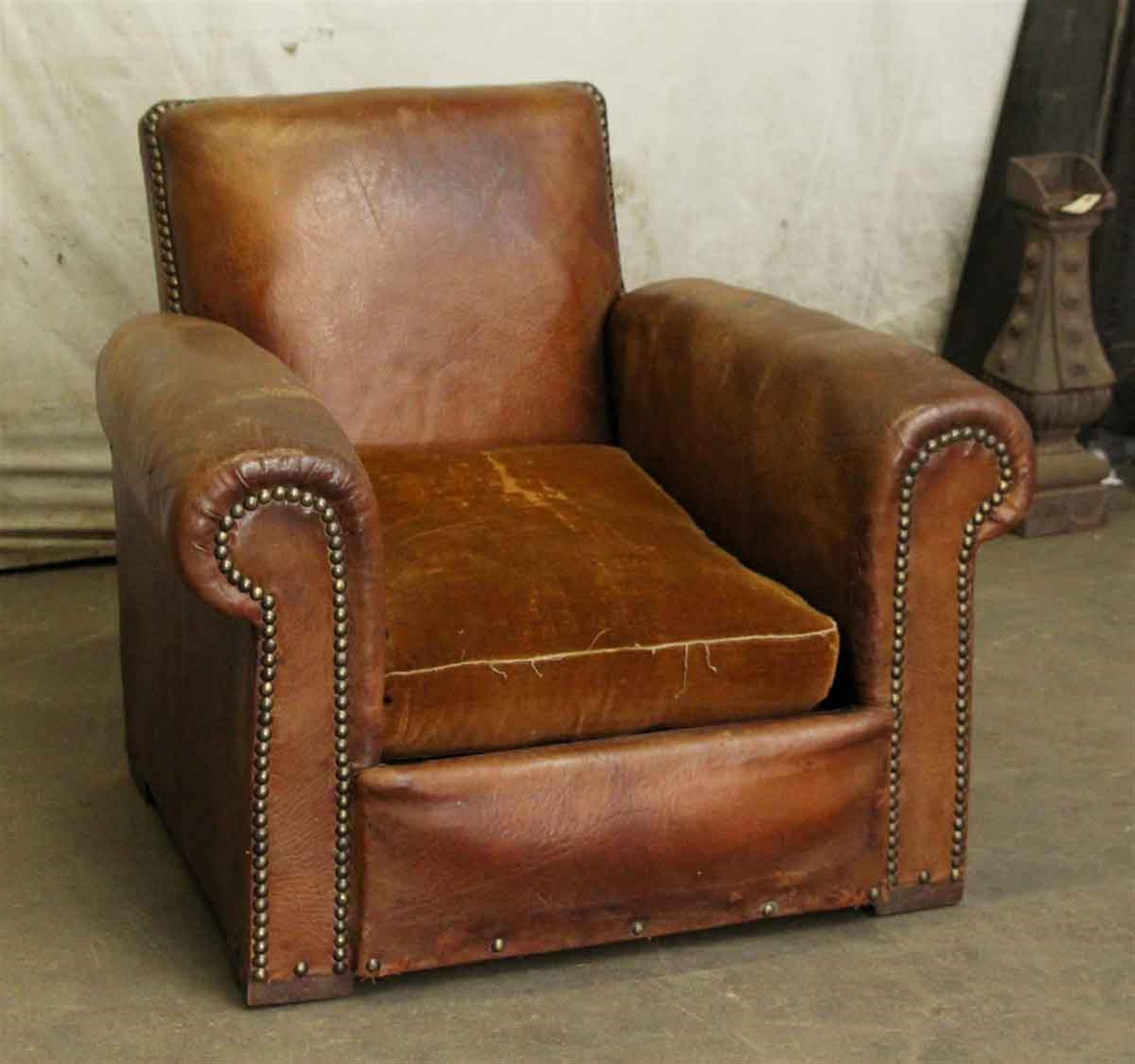 Pair of French beefy leather club chairs with feather filled cushions from the 1980s. Featuring brass studs along the front seams in front and around the back. The cushions are worn with fraying on the edges. These can be seen at our 91 8th Ave