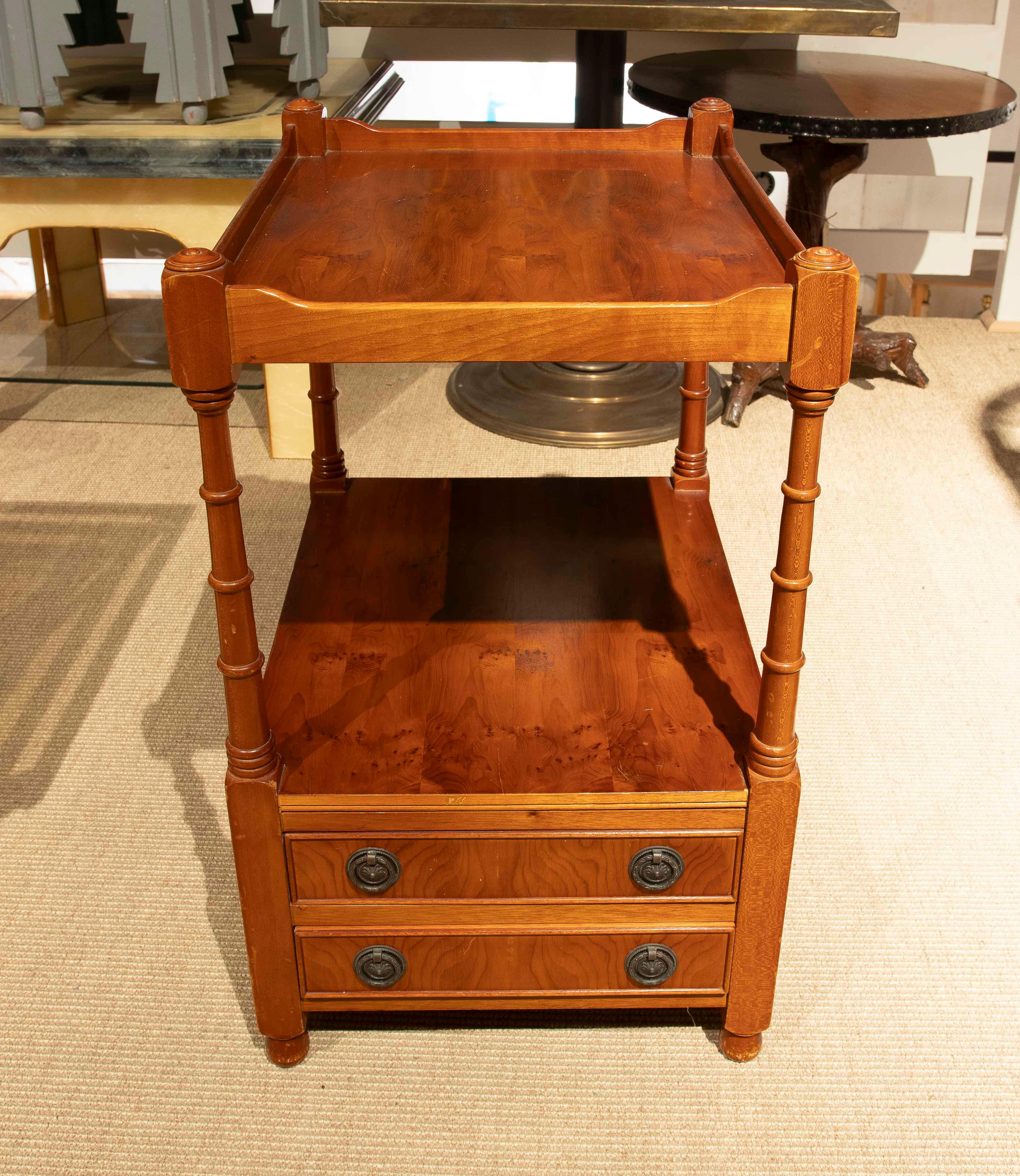 Elegante par de mesas auxiliares vintage, de madera con un cálido acabado natural. Su diseño estructurado en dos niveles incluye una bandeja superior con bordes elevados y un estante intermedio, que aportan funcionalidad y estilo. La base tiene dos