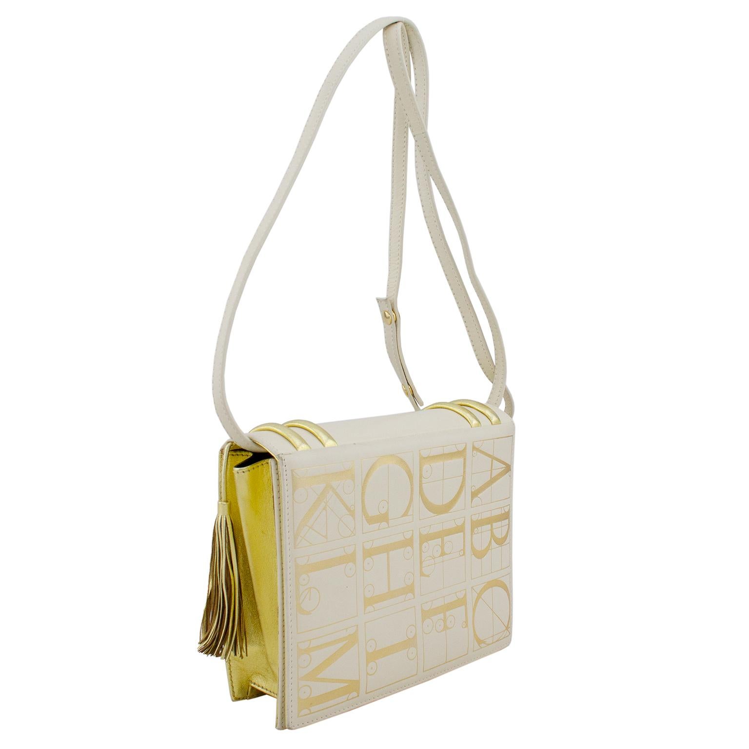 1980s Paloma Picasso cream leather evening purse with gold details and tassel. Front and back features the alphabet in large gold letters and mirrors the cover design of a whimsical faux library book. The fantasy shape adds a touch of humor and