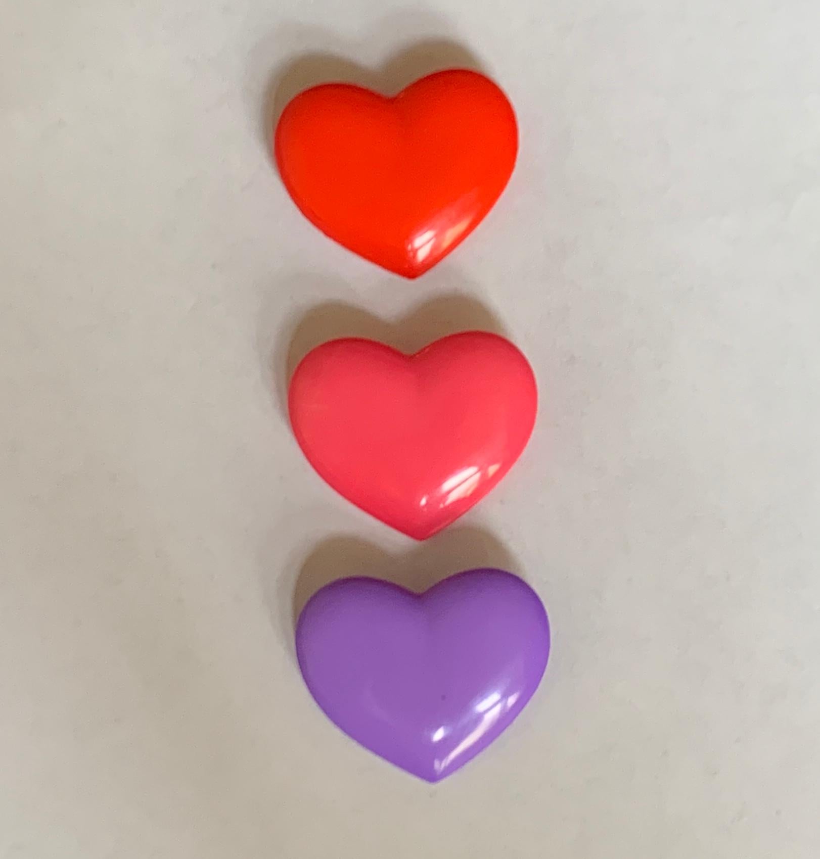 Set of three Patrick Kelly for Streamline vintage 1980s plastic heart shaped buttons in pink, red, and purple. Single loop at back for threading. (You could also glue a brooch backing on to use the buttons as pins, just like Patrick did!)

Signed