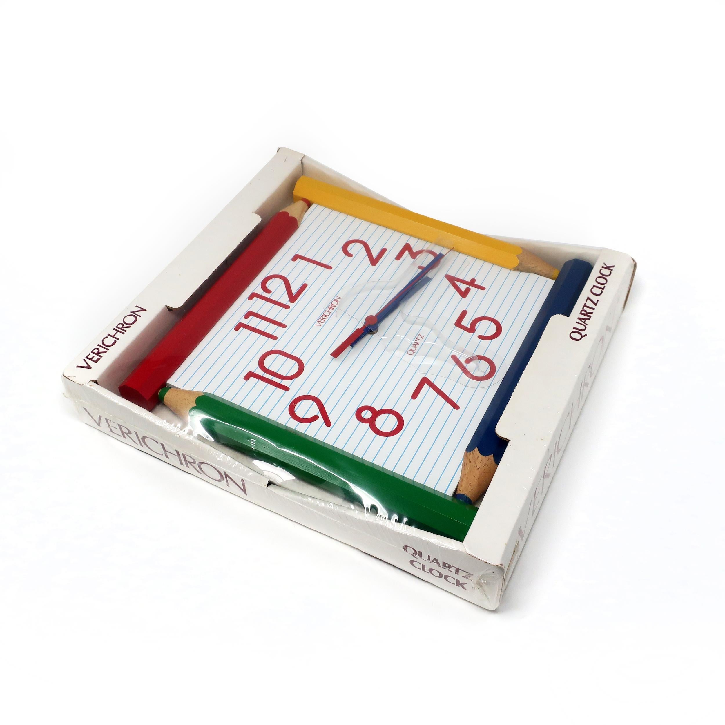 A fun 1980s wall clock by Verichron (a Harris & Mallow brand) with a face that resembles lined notebook paper, a four-colored wooden pencil frame, red numbers in a 1970s/80s font, and blue and red hands.  Bright, primary-colored, and whimsical. 