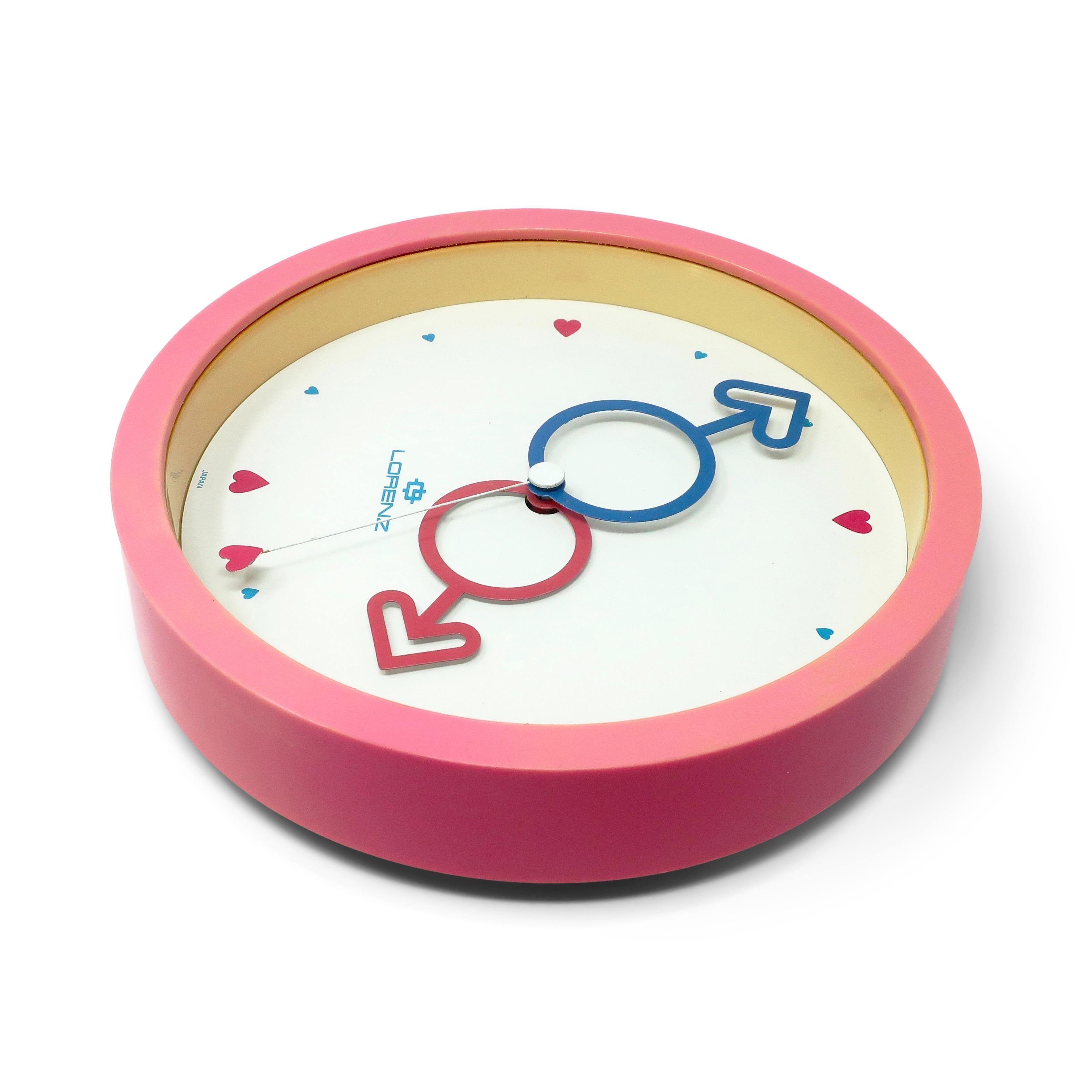 Eine lustige runde postmoderne Lorenz Wanduhr mit mehrfarbigen Akzenten aus Japan.  Rosa Gehäuse, weißes Zifferblatt, rote und blaue Herzzeiger, roter Herzsekundenzeiger und rote und blaue Herzen als Zahlen.  Hell, farbenfroh und lustig, und es
