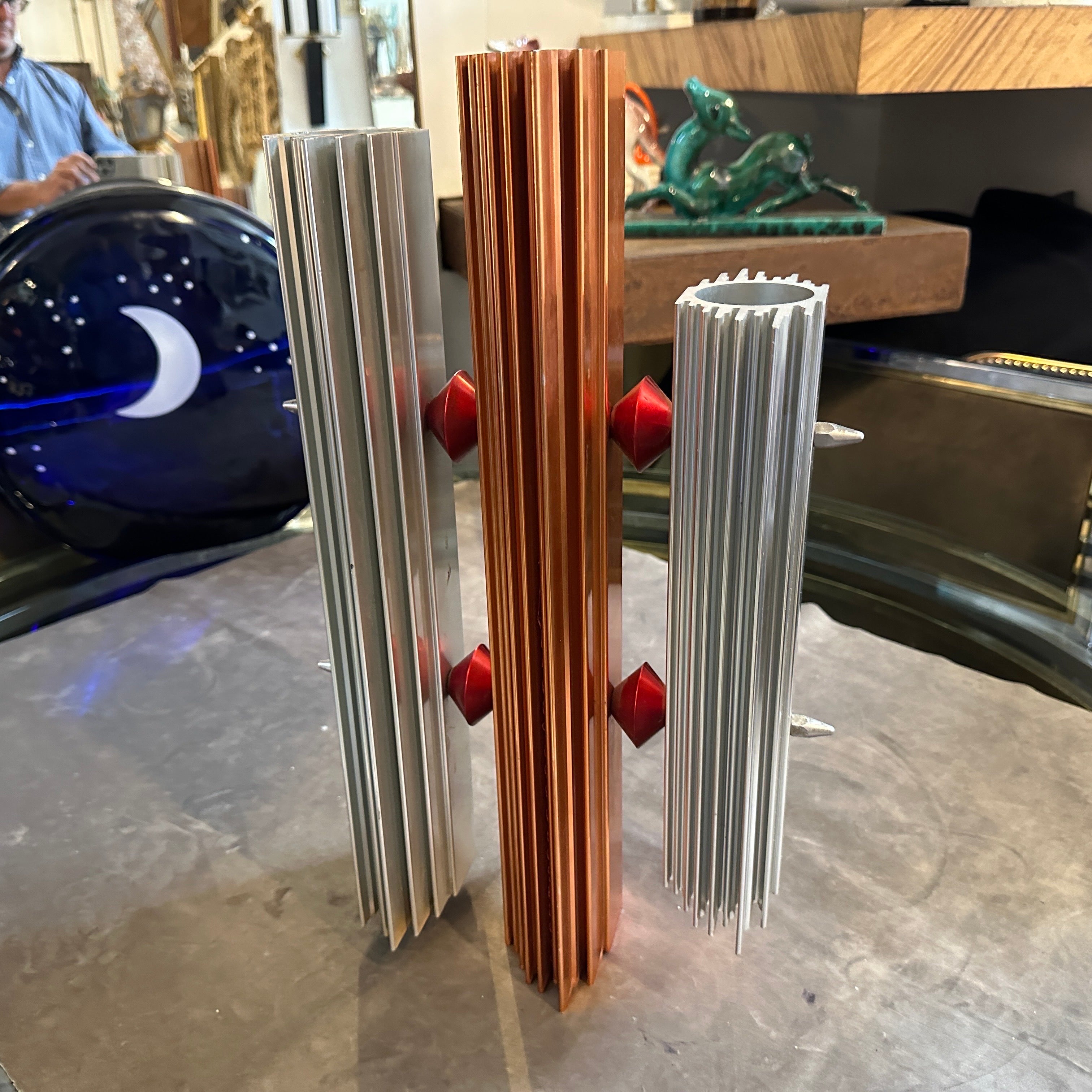 Questa particolare scultura italiana Post Modern degli anni '80 incarna lo spirito audace e provocatorio di un'epoca cruciale per il design. Tre elementi verticali distinti attirano l'attenzione: due realizzati in alluminio scintillante, le cui