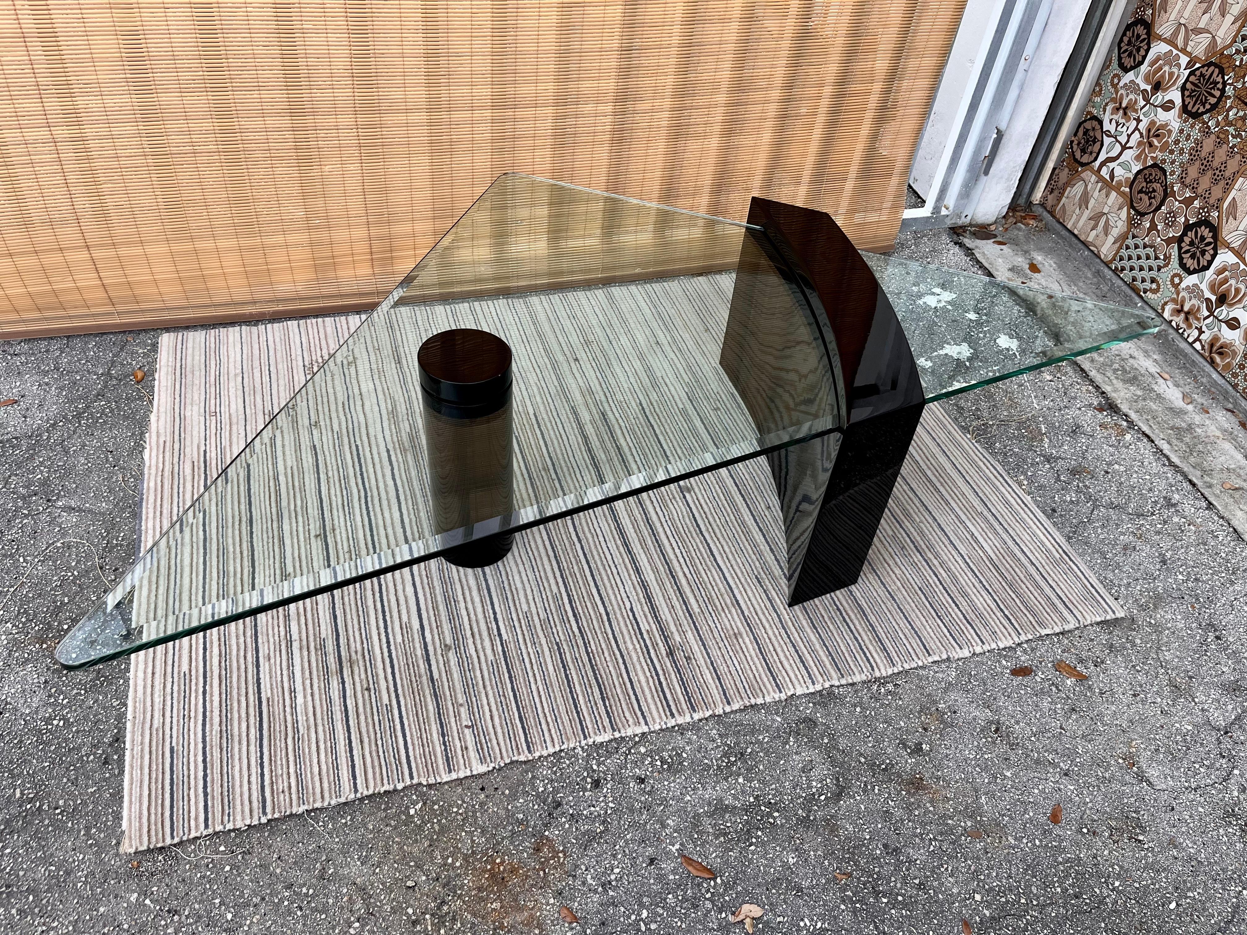 Vintage, large scale post modern sculptural Black Lacquer Coffee Table with a Triangular Glass top in the of Roger Rougier's Style. Circa 1980s. 
Features a glossy lacquered six inches round column and a curved pedestal with a slot that takes the