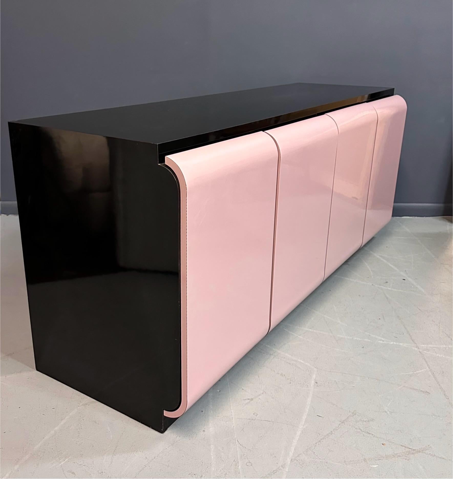 The quintessential Post modern credenza in black and pink laminate. This piece has four large doors and behind them are two generous storage compartments each with a adjustable shelf and the left hand compartment has a drawer.