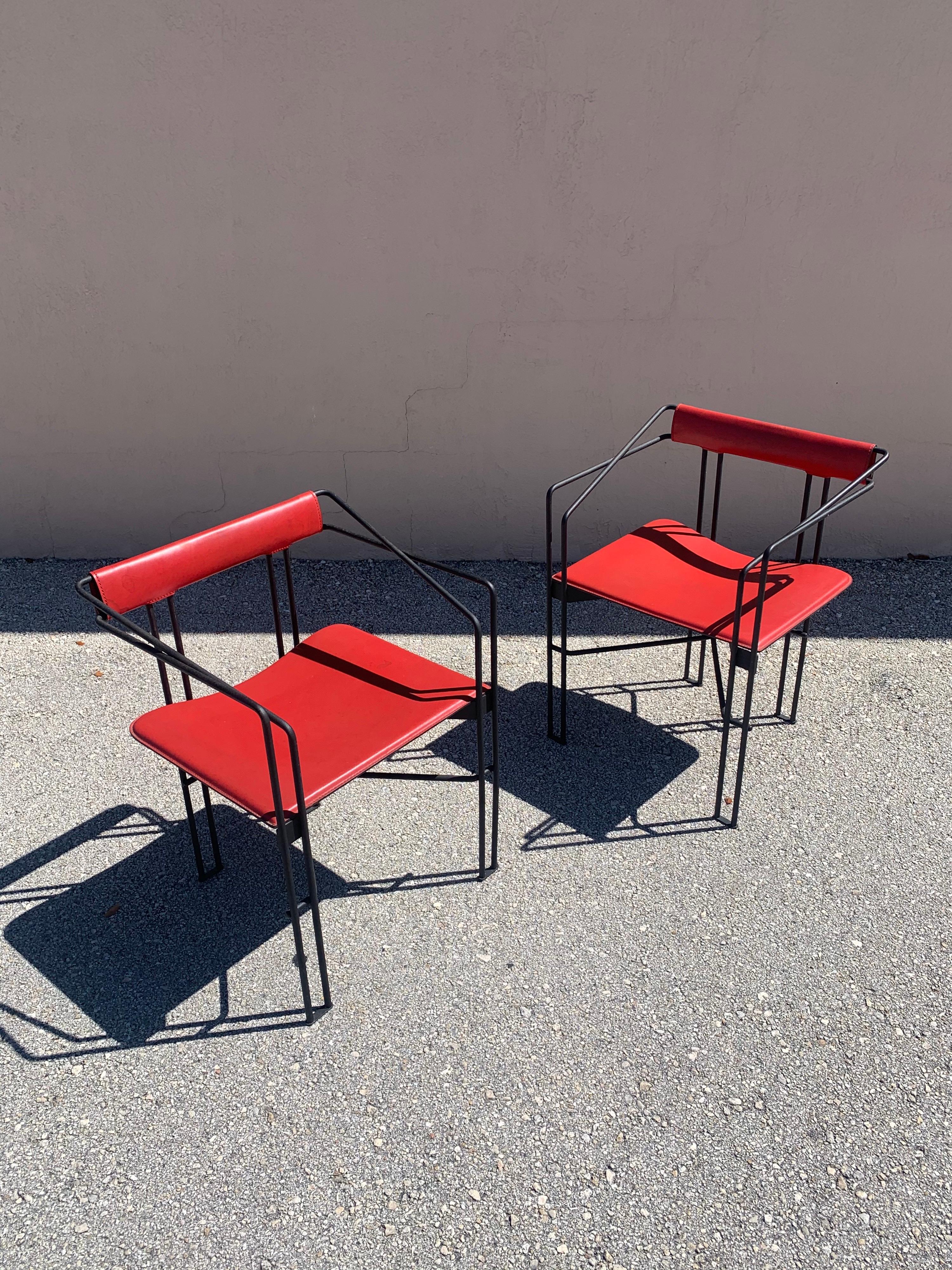 Stunning pair of post modern arm chairs in leather and iron. Thick red leather seats and back rest. Geometric wrought iron frames. Creating a striking pair of chairs.
