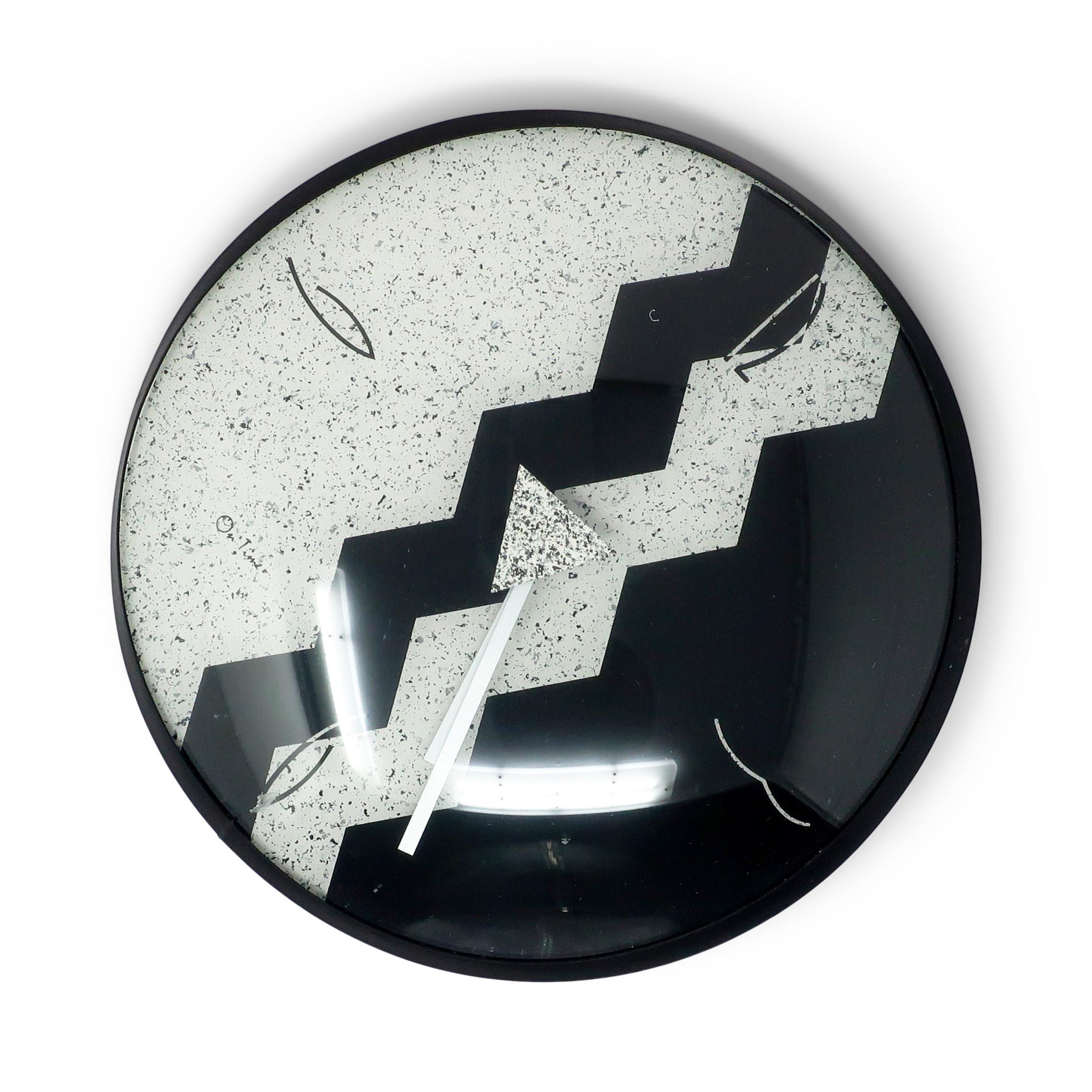 Un reloj de pared postmoderno vintage de los años 80, de Empire Art Products. La esfera del reloj tiene varios tonos de negro, blanco roto y plata con formas geométricas.

En buen estado vintage con desgaste acorde con la edad y el uso. Funciona con