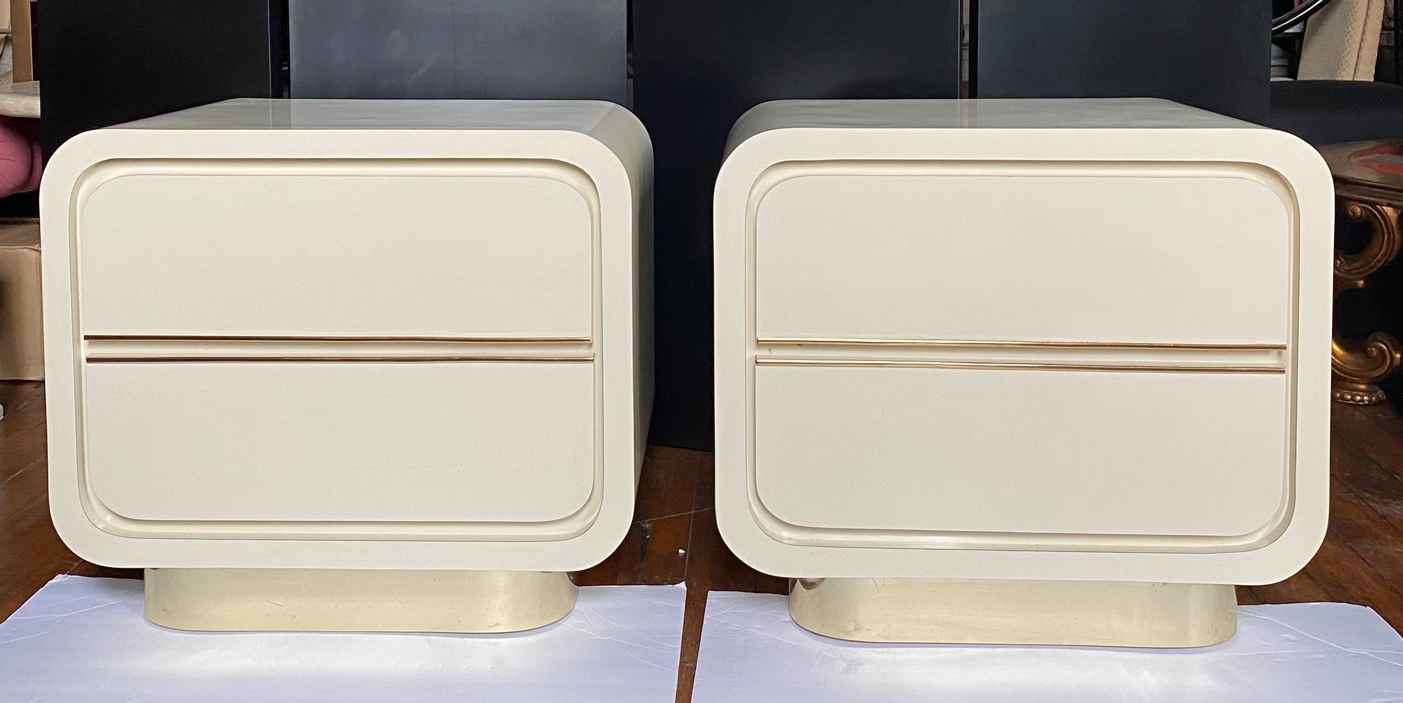 Pair of Post Modern two drawer cream gloss lacquer nightstands. These sculptural Art Deco style bedside tables feature a cream gloss laminate and reflective gold trim. In the style of Karl Springer.