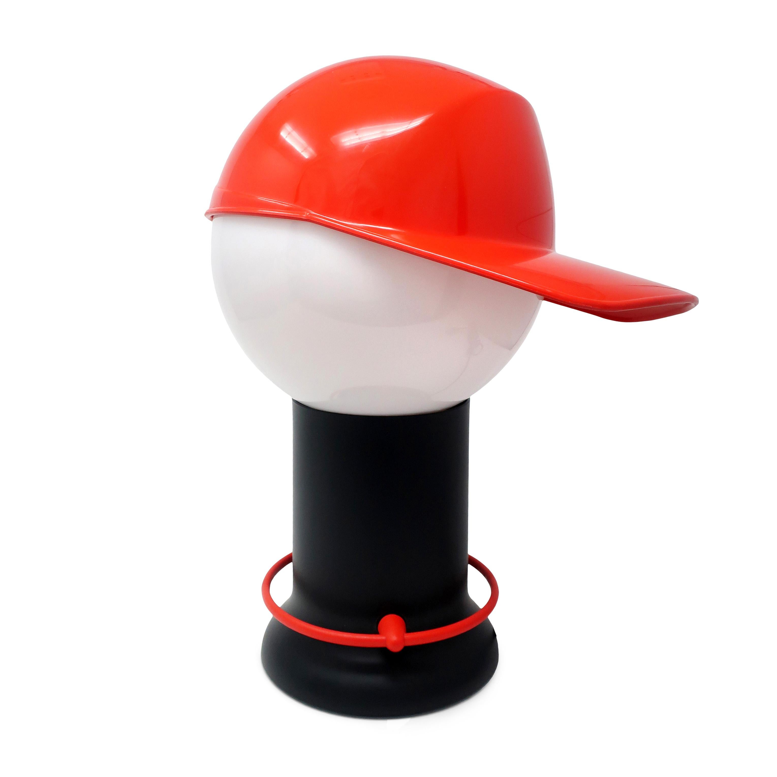 A fantastic postmodern 1980s “Cap” table lamp by Giorgetto Giugiaro for Bilumen. A red baseball hat sits on a white globe shade, which in turn sits on the black base. On/off switch is a red plastic circle around the base that pivots when pressed to