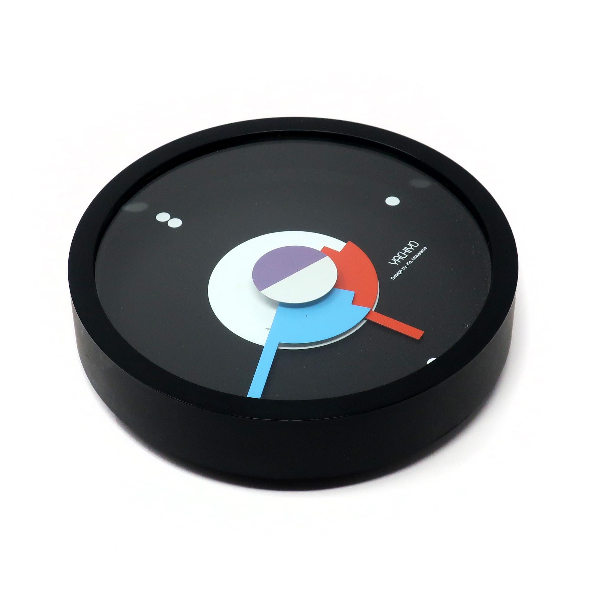 An outstanding round postmodern wall clock designed by Ko Mizuyama, a prolific Japanese designer of clocks in the 1980s.  It has a black plastic case, black face with dots for numbers, and graphical red, purple, white, and blue hands.

In good