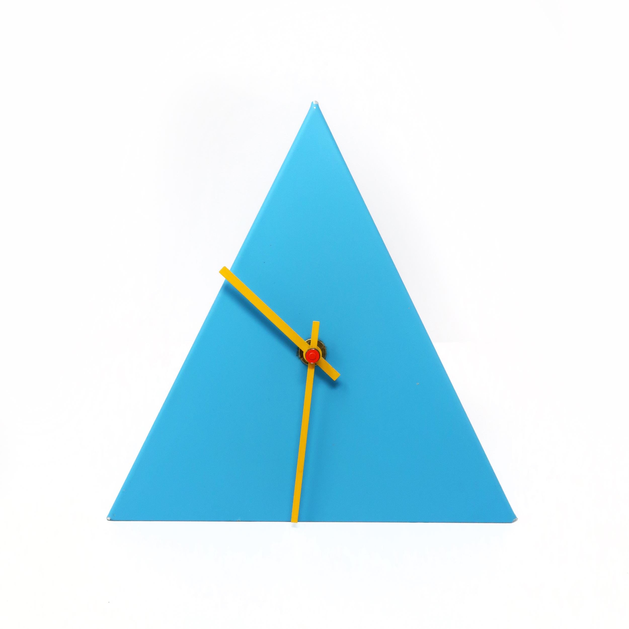 An eye-catching postmodern blue metal desk, table, or mantle clock in the shape of a pyramid with yellow hands and red accent. 

In vintage condition with wear consistent with age and use, including marking on tip of the pyramid and missing second