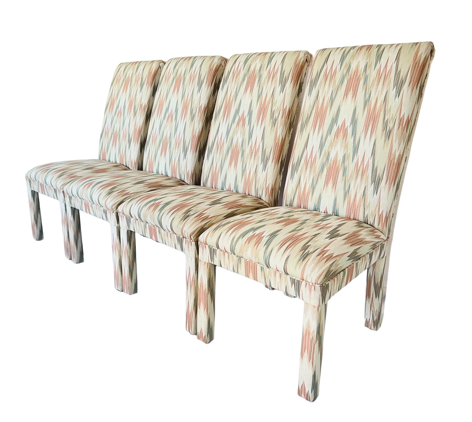 A late 20th century set of four postmodern style Parsons dining side chairs. Featuring a high back and curved scroll top with button detail. Fully upholstered in heavy woven jacquard flamestitch fabric in shades of soft pink, teal, beige &