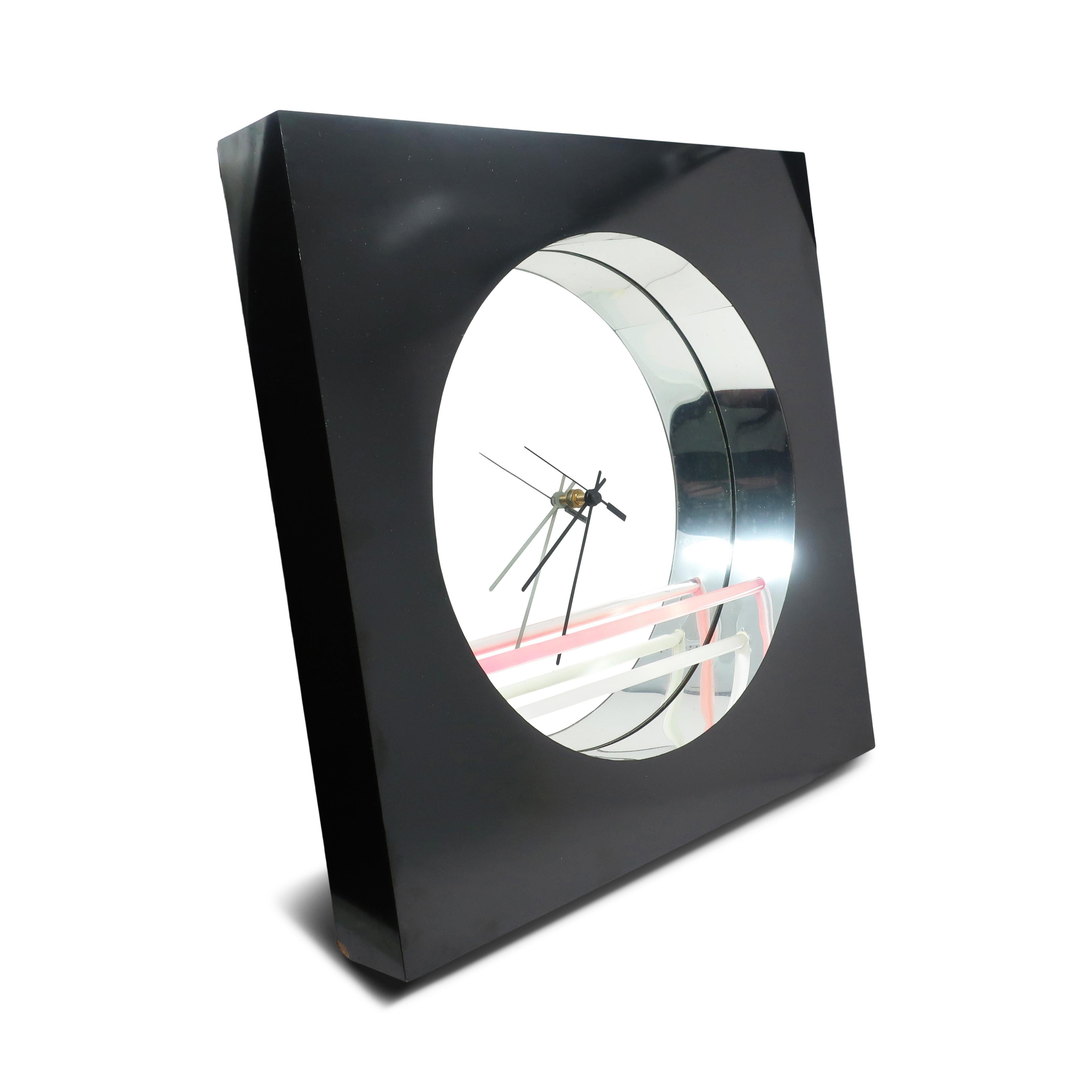 Un bellissimo orologio a specchio da parete disegnato da Jon Gilmore per Accessory Art Studio, probabilmente negli anni Ottanta.  Con una cassa in legno rivestita in laminato nero, un quadrante rotondo a specchio incassato, lancette nere e accenti