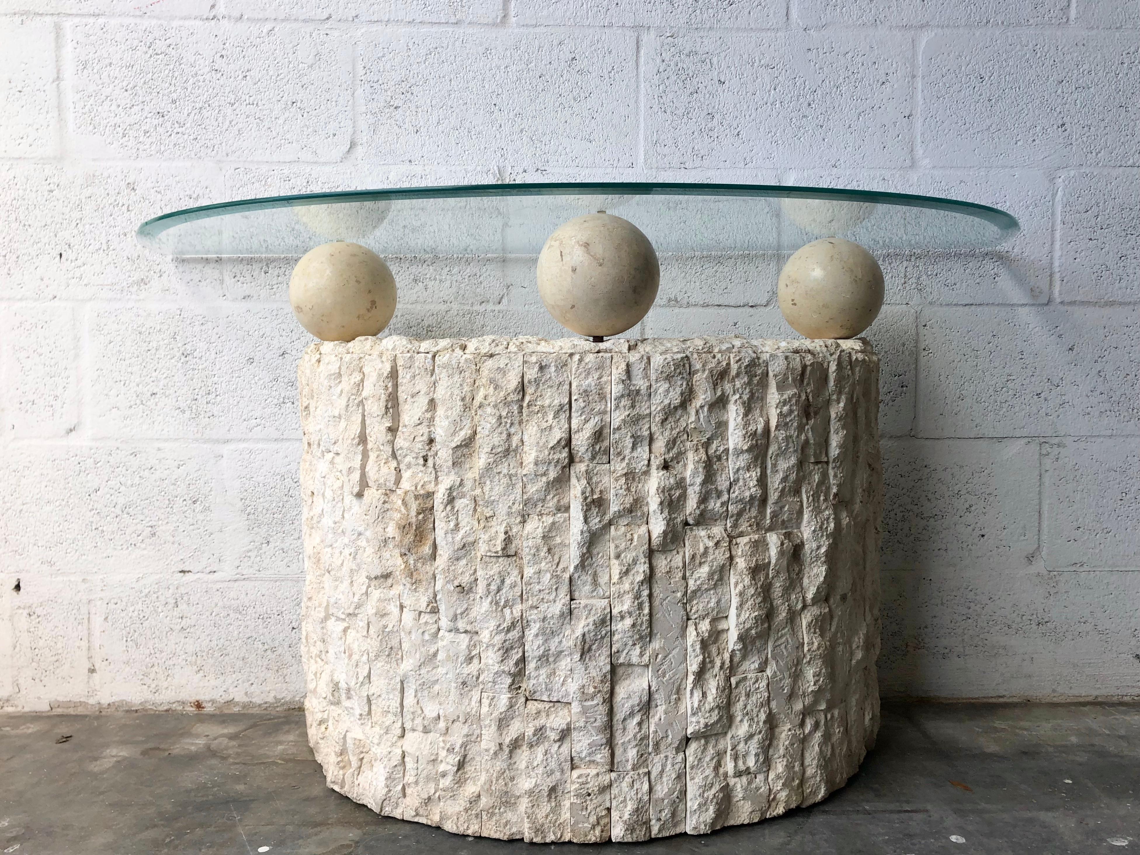 Vintage Postmodern natural mactan stone console /sofa table. Circa 1980's 
Features a half round beveled glass top resting on a fractured Mactan Stone facade pedestal with three smooth tessellated orbs. 
Although this piece looks heavy and