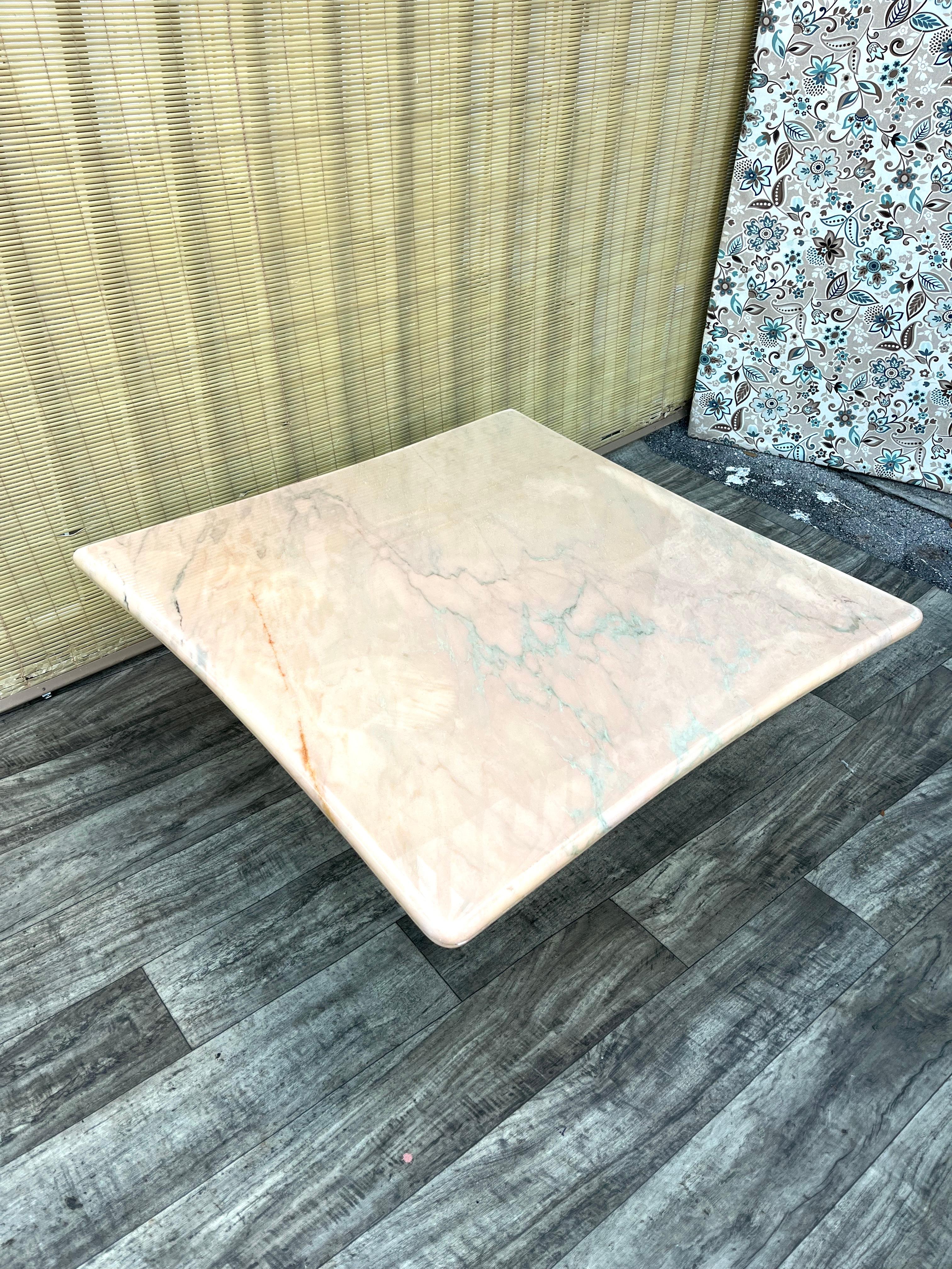 Mesa de centro vintage postmoderna de mármol rosa. Alrededor de 1980 
Presenta una parte superior cuadrada con bordes cóncavos y un suave color rosa con preciosas vetas de piedra de mármol natural en suaves tonos azules, naranjas y marrones. 
La