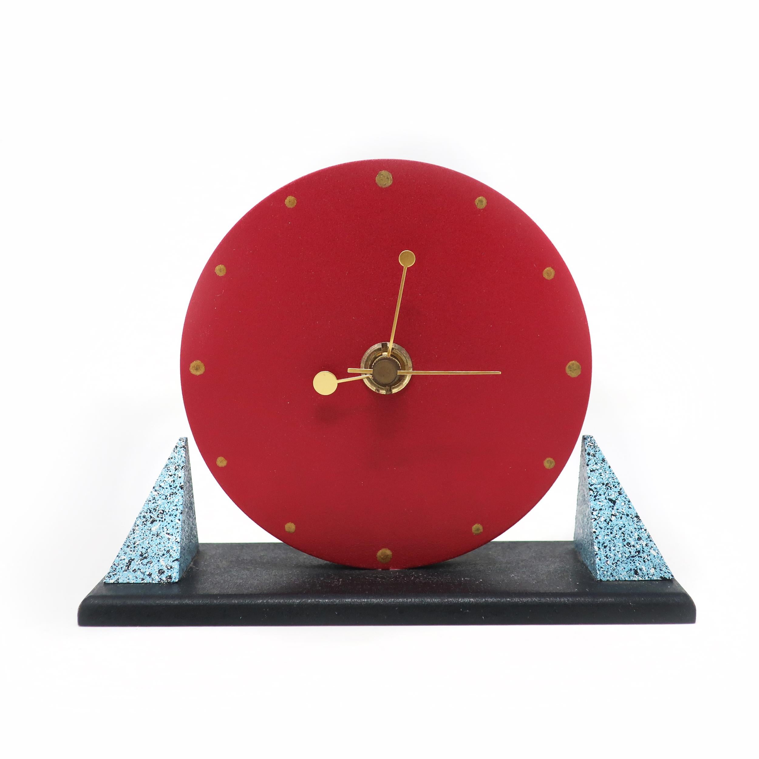 A sophisticated yet adorable postmodern desk clock with a red face, blue speckled triangular supports, black base, and brass hands and numbers. Made in Japan and in very good vintage condition with wear consistent with age and use.

Measures: 6