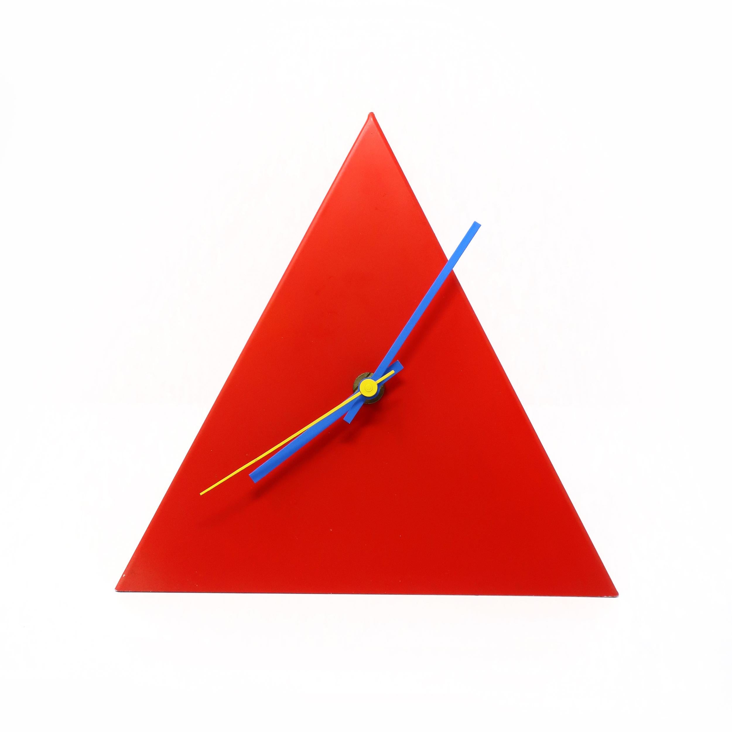 An eye-catching postmodern red metal desk, table , or mantle clock in the shape of a pyramid with blue and yellow hands. 

In vintage condition with wear consistent with age and use, including marking on tip of the pyramid.

Measures: 8