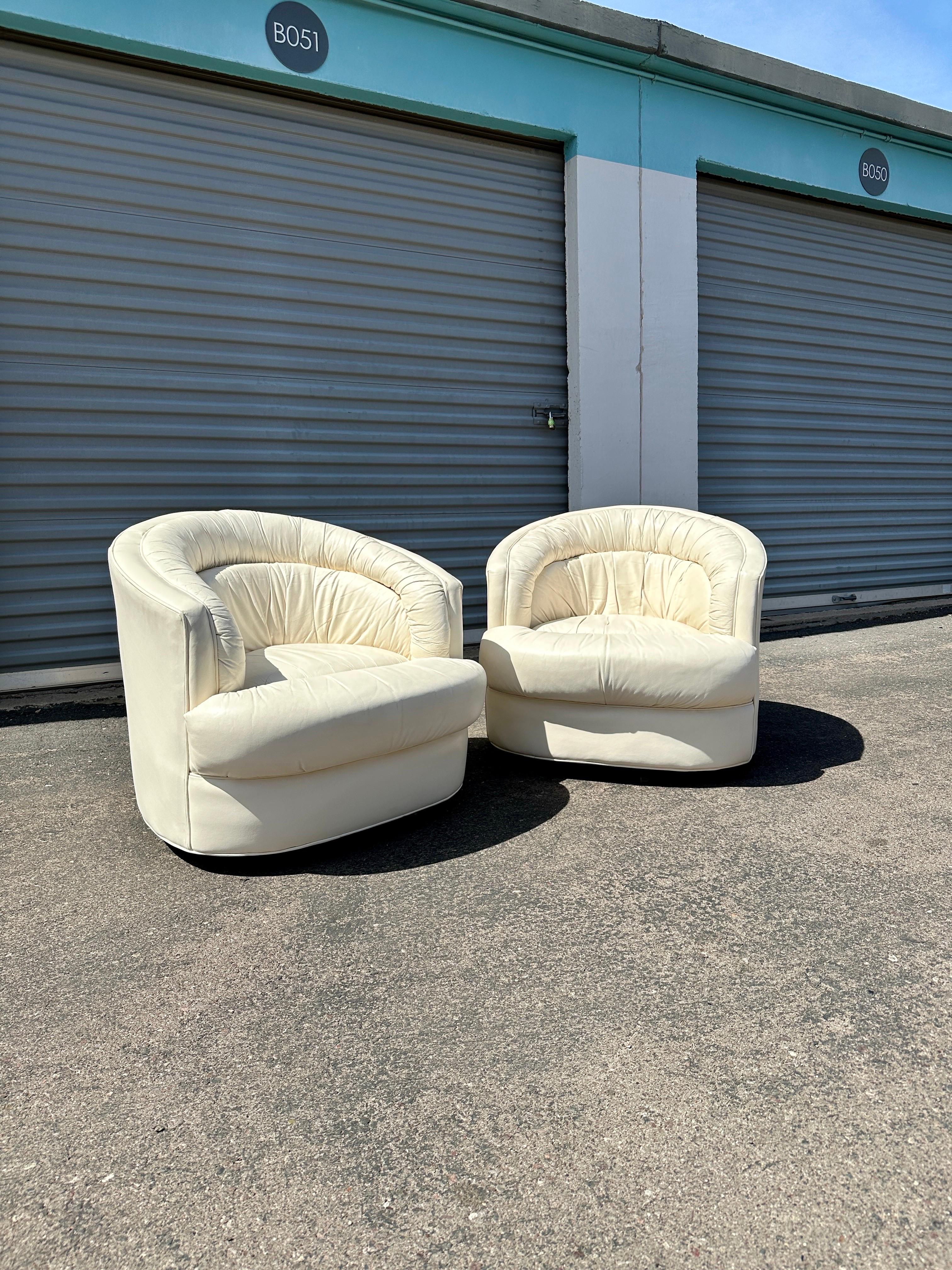 This sculptural pair of 1980s swivel lounge chairs channels the plush, curvilinear glamour of postmodern design at its peak. Upholstered in creamy top grain leather by Emerson Leather, each chair features a fully upholstered frame, low profile, and