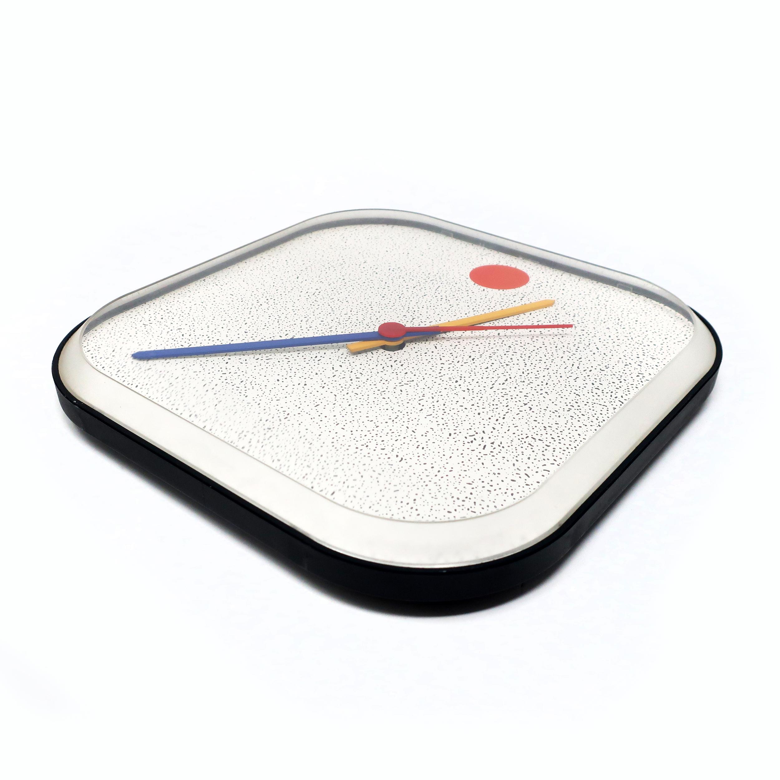 A 1980s vintage IKEA wall clock with all of the hallmarks of postmodern and Memphis-inspired design: white speckled clock face, primary colored hands, and square shape with rounded corners. Cleverly, the round red dot that one would assume is for 12