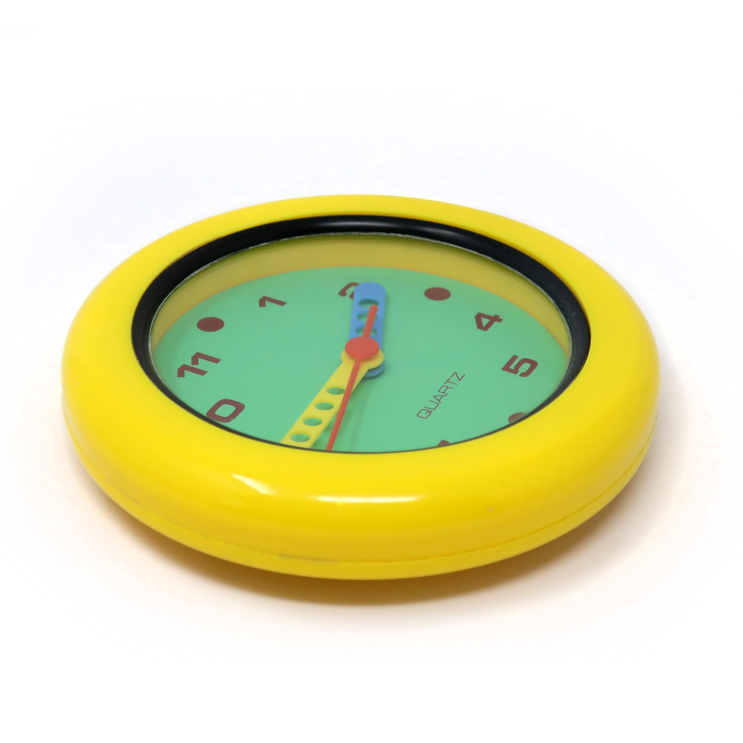 A 1980s wall clock with all of the hallmarks of postmodern and Memphis-inspired design: yellow case with black trim, green face, hands in blue, yellow and red, and black numbers.

In very good vintage condition with wear consistent with age and