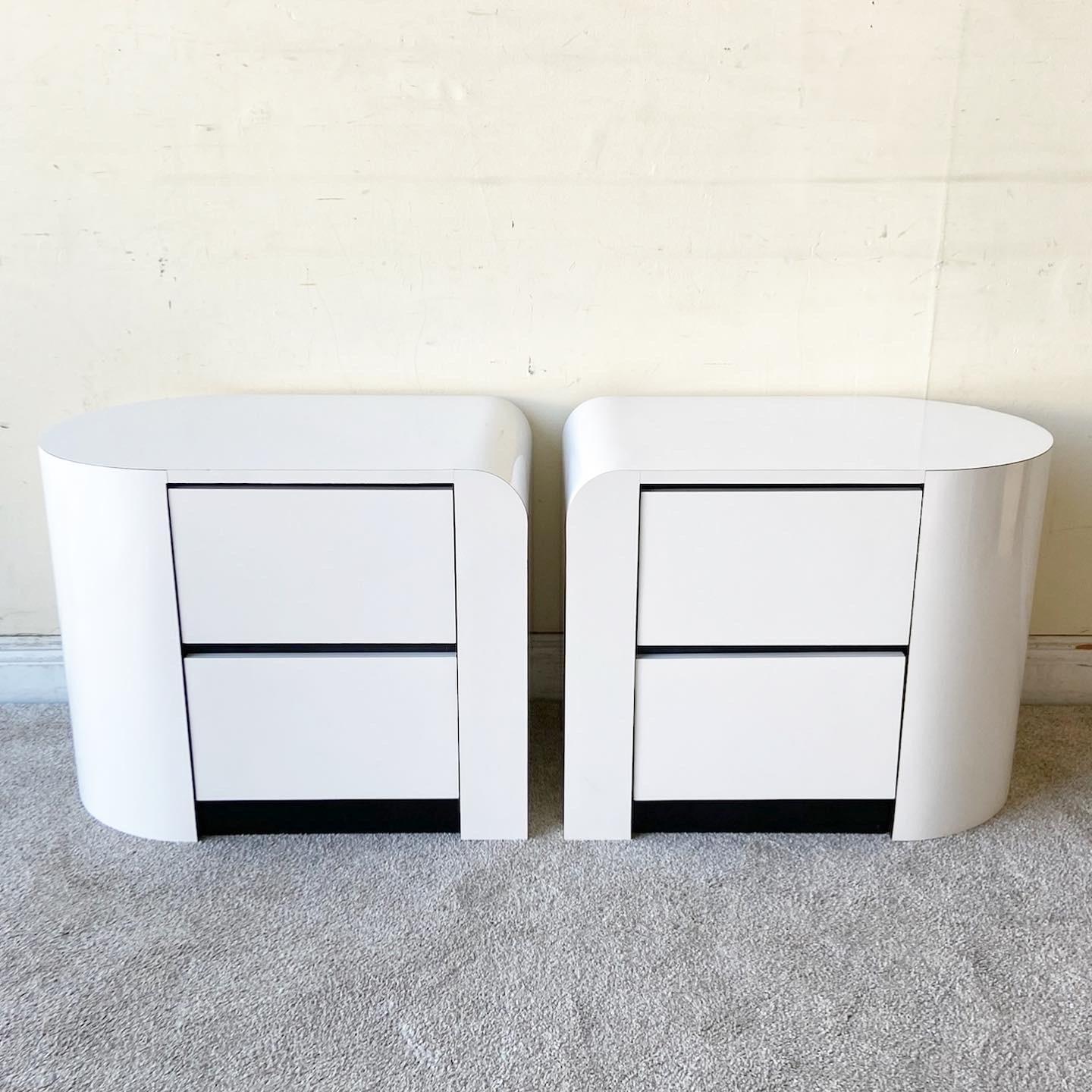 Amazing vintage postmodern pair of nightstands. Each feature a white lacquer laminate with black laminate bordering the drawers. A unique construction displays a waterfall edge on one side and the other side half rounded. 