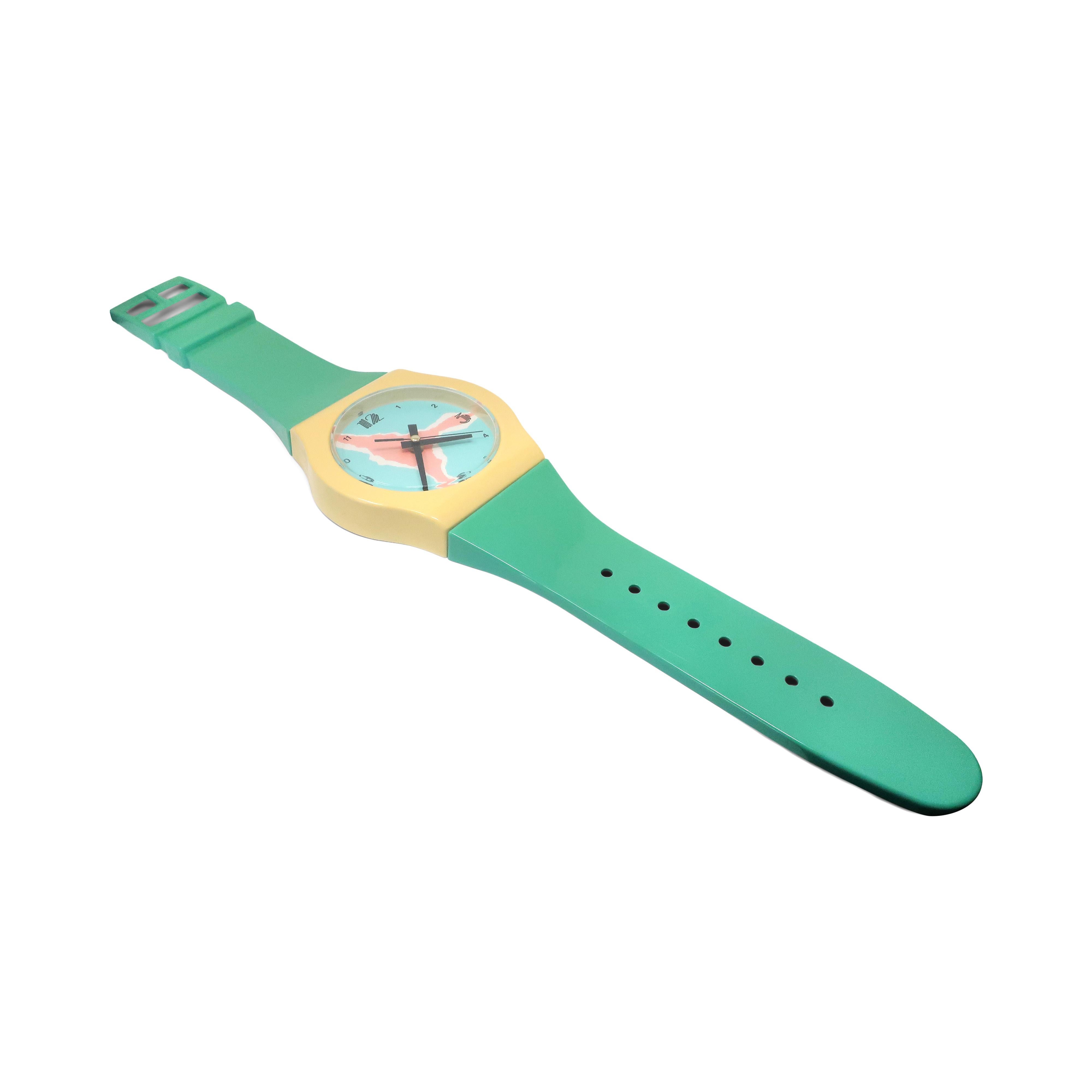 A fantastic vintage 1980s green, yellow, and pink wrist watch wall clock, in the vein of Swatch’s great designs. With a green band, yellow bezel, turquoise and pink face, and black hands, this is a stunner! In good vintage condition with wear