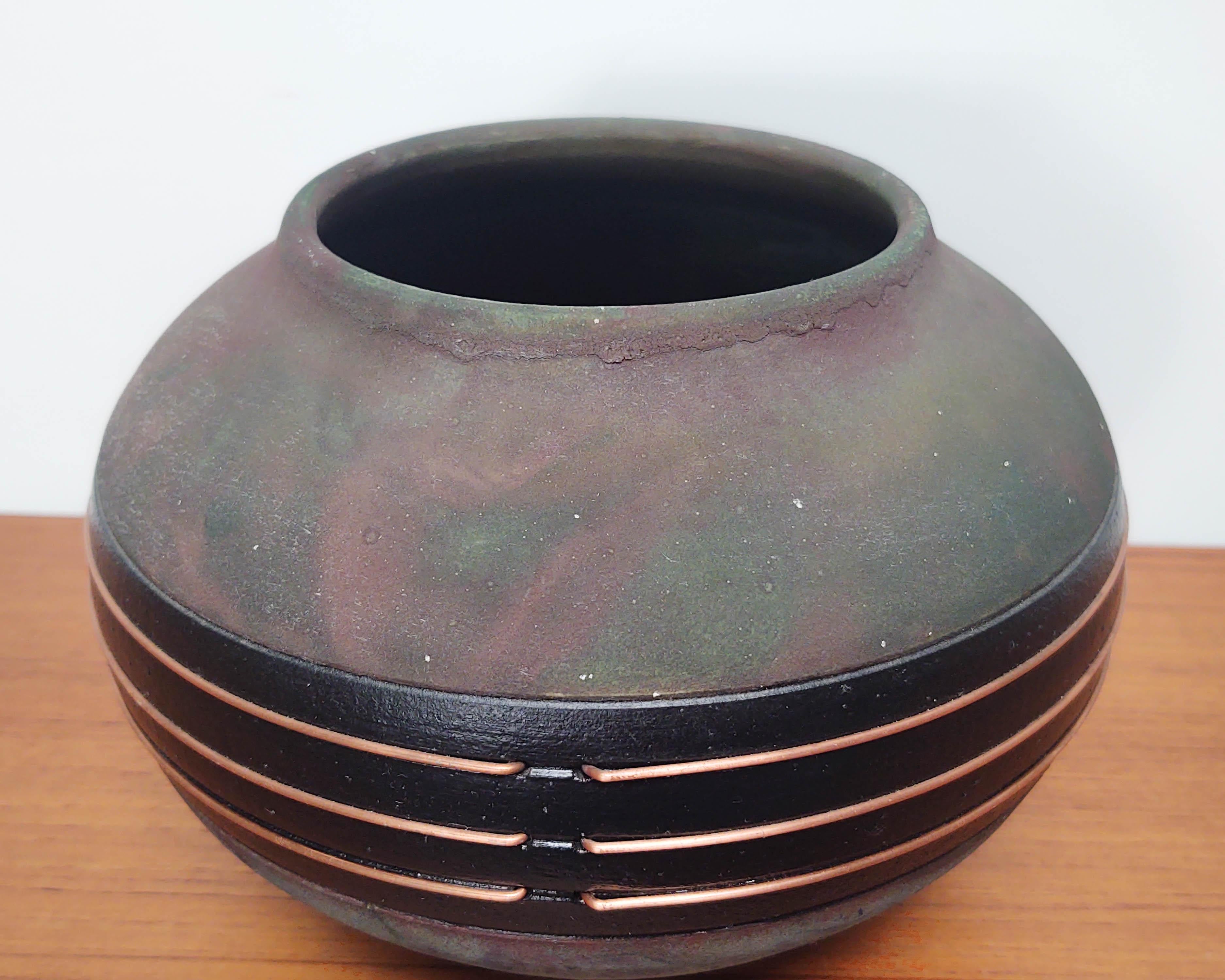Oblong black ceramic vase / vessel with swirling rainbow oxide coating typical of raku firing. Copper wire decorations are integral to the vessel. Not watertight, typical of earthenware. Signed on bottom.
 
6