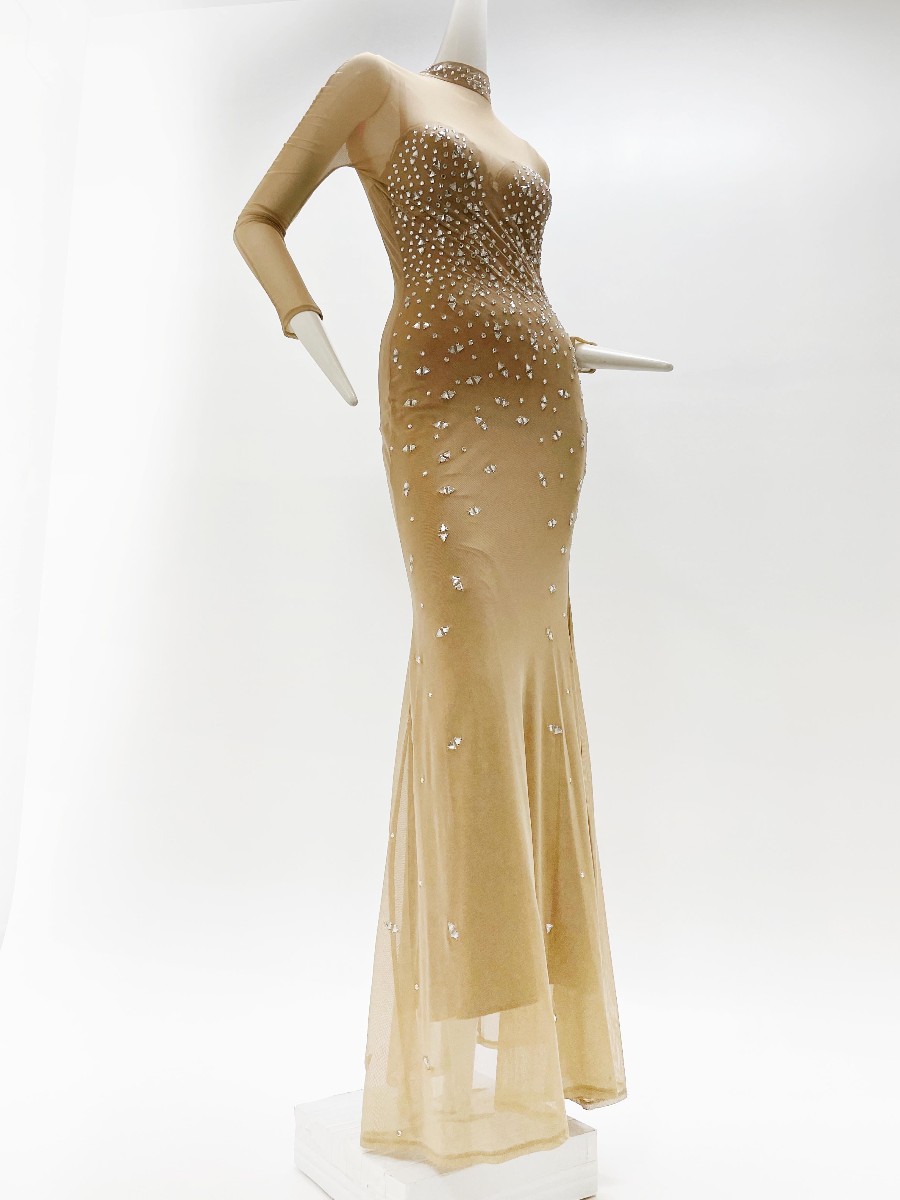A sexy 1980s nude stretch tulle gown embellished all over with triangular and round-set prong rhinestones. Lining has a sweetheart neckline and zips at back. Top sparkling layer has a flared hemline, high neckline and slight Dolman sleeves. Fits a