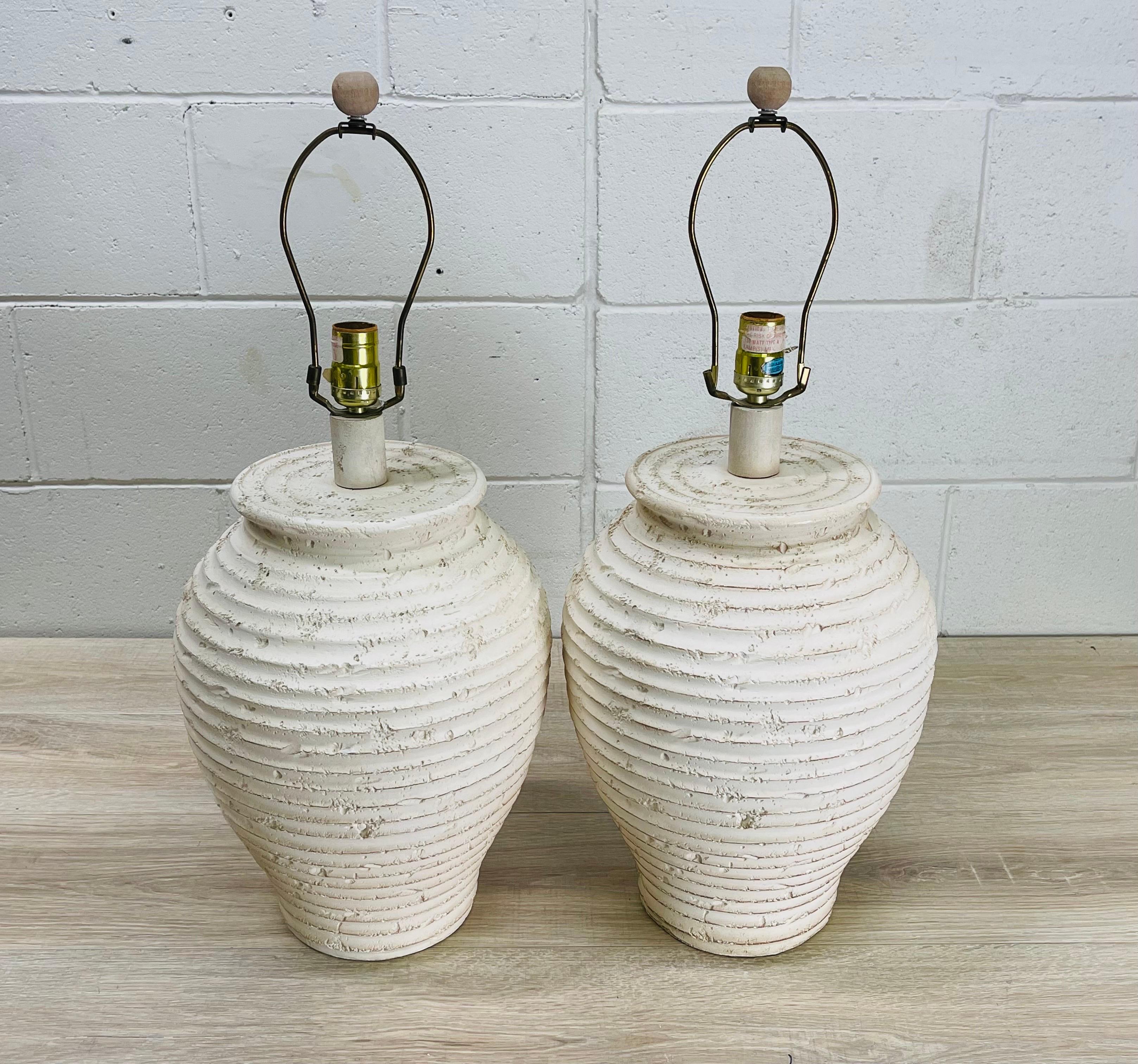 Vintage 1980s pair of ribbed white pottery table lamps. The lamps are wired for the US and in working condition. The lamps have a ribbed design and texture all over. The lamps use a standard 100W bulb. Measures: Socket, 19.5” H. Harp, 4” Diameter x