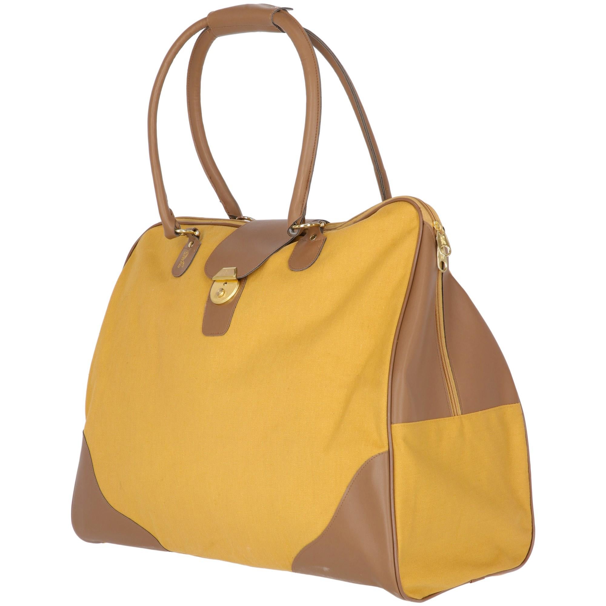 Roberta di Camerino mustard colored cotton travel bag with brown faux leather inserts and handles. With zip fastening and front buttoned closure with keys, with outer zip pocket on the back. Logo detail is on the pullers and embroidered in golden