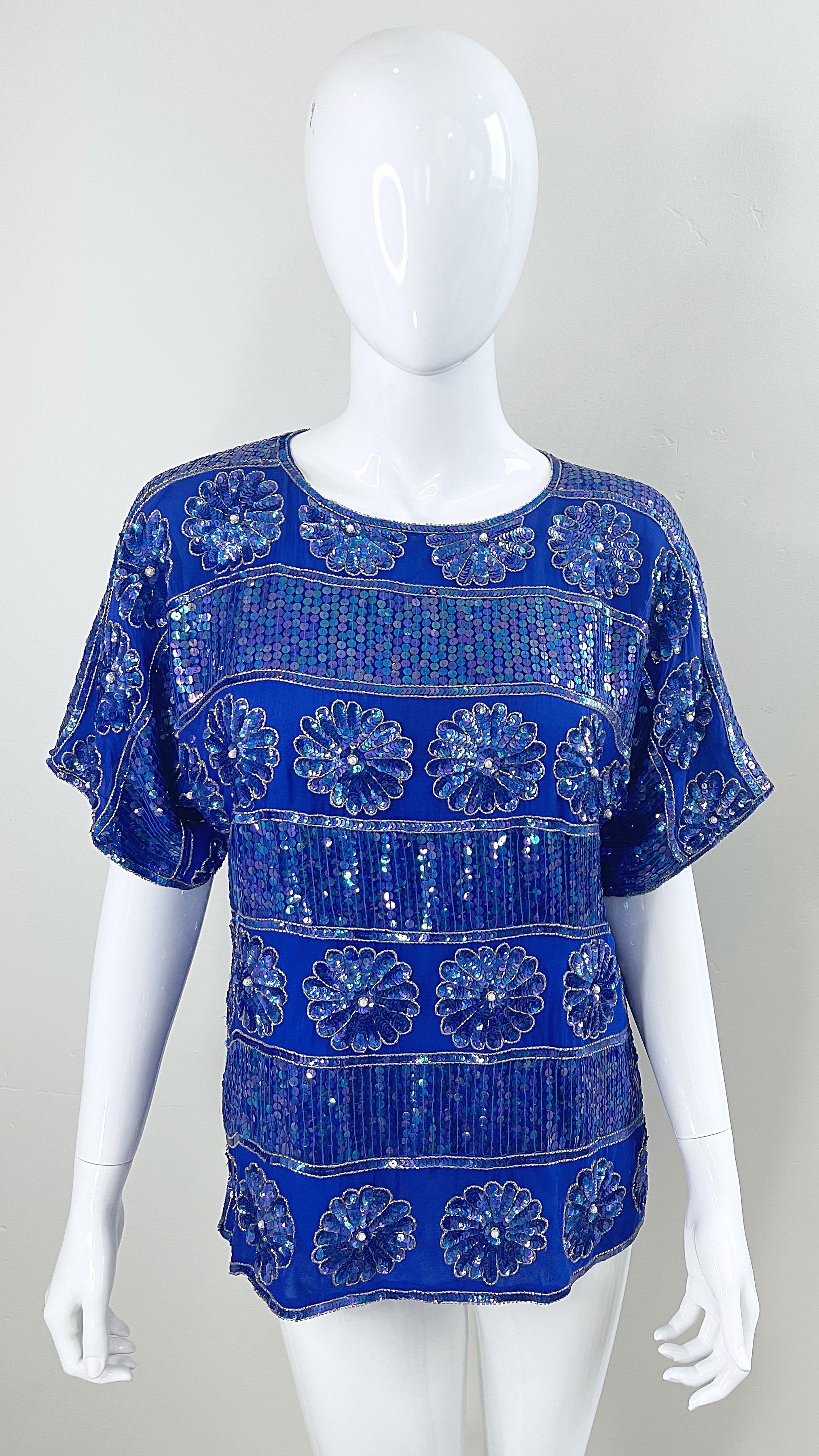 Amazing 1980s royal blue silk chiffon short sleeve blouse ! Features thousands of hand-sewn sequins, beads and pearls throughout. Sequins sewn to look like flowers. Hook-and-eye closure at top back center neck. The perfect top for any occasion !
In