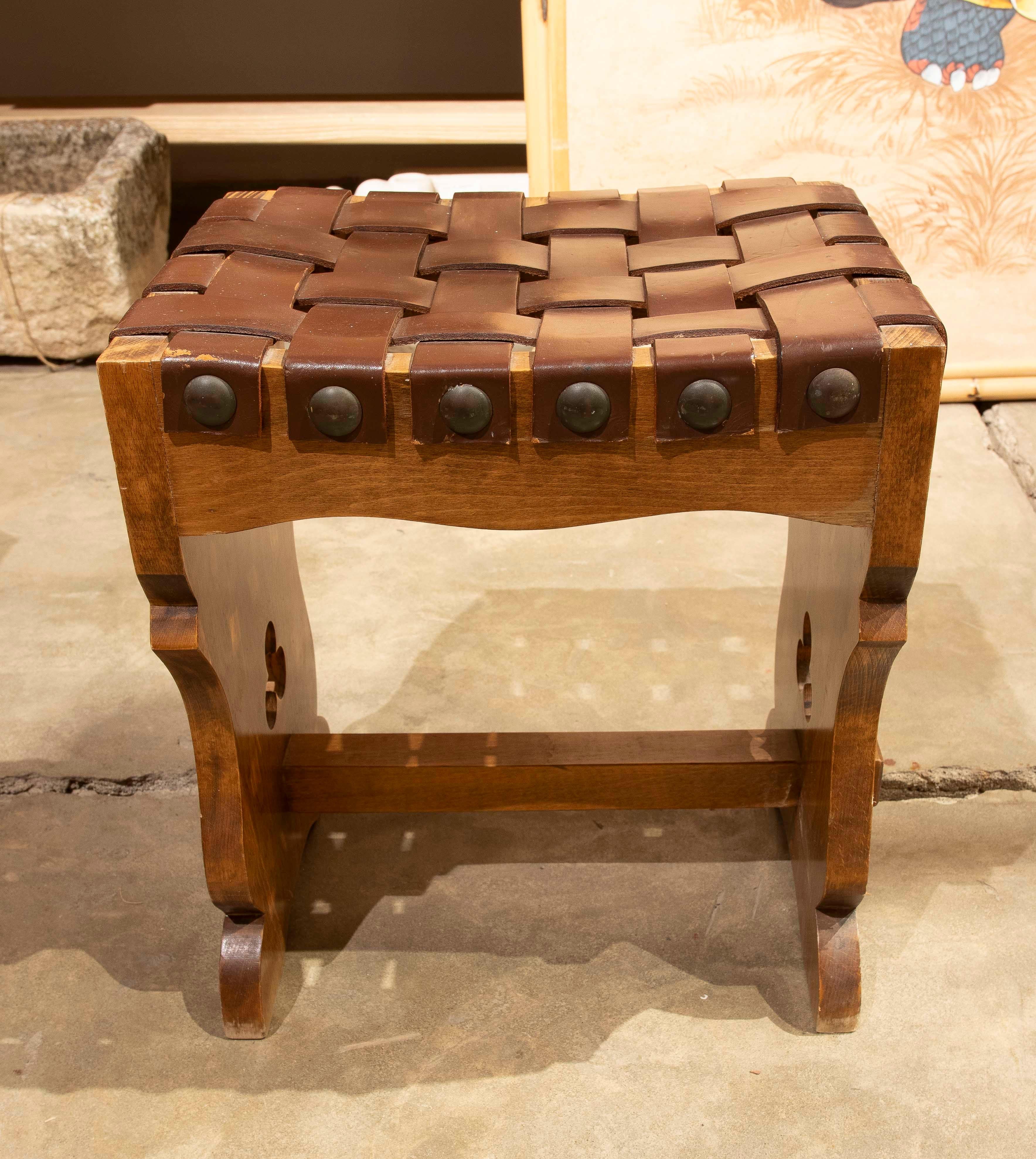 Elegante sgabello in stile rustico realizzato in legno massiccio con seduta in pelle intrecciata a mano. Il suo design robusto e i dettagli intagliati sulle gambe evocano la tradizione artigianale, mentre i rivetti in metallo incorniciano la pelle,