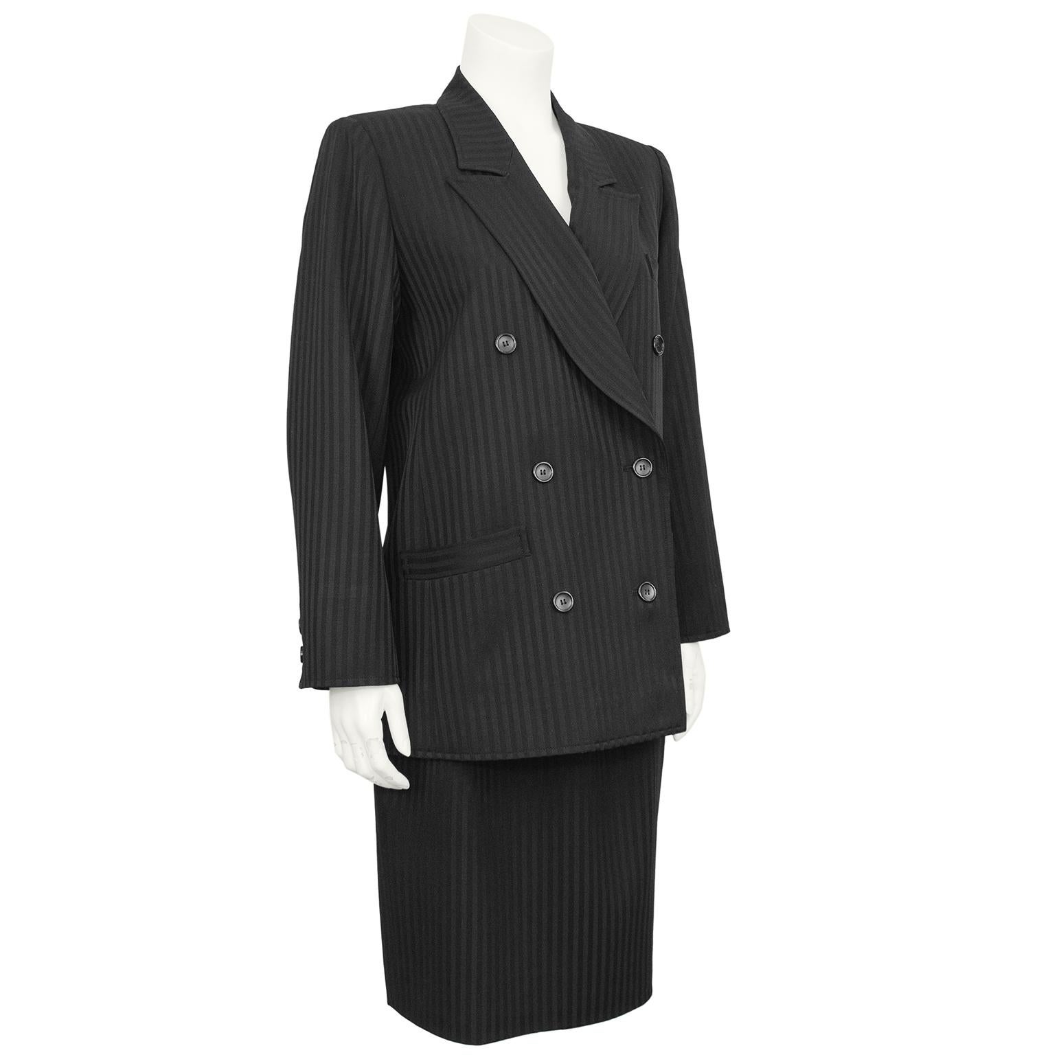 1980s classic Saint Laurent Rive Gauche label black pinstripe skirt suit. The double breasted blazer is a staple of Saint Laurent collections, structured and menswear inspired. The jacket has a notched lapel, two pockets on the hips and one on the