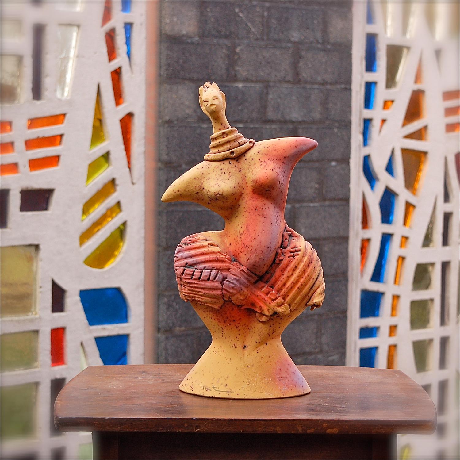 Expressive and colourful sculpture of a female figure, possibly a fertility statue. The imagery and style date it to the 1980s. The figure is made from earthenware, coloured in bright yellow, orange and purple with a textured surface that is still