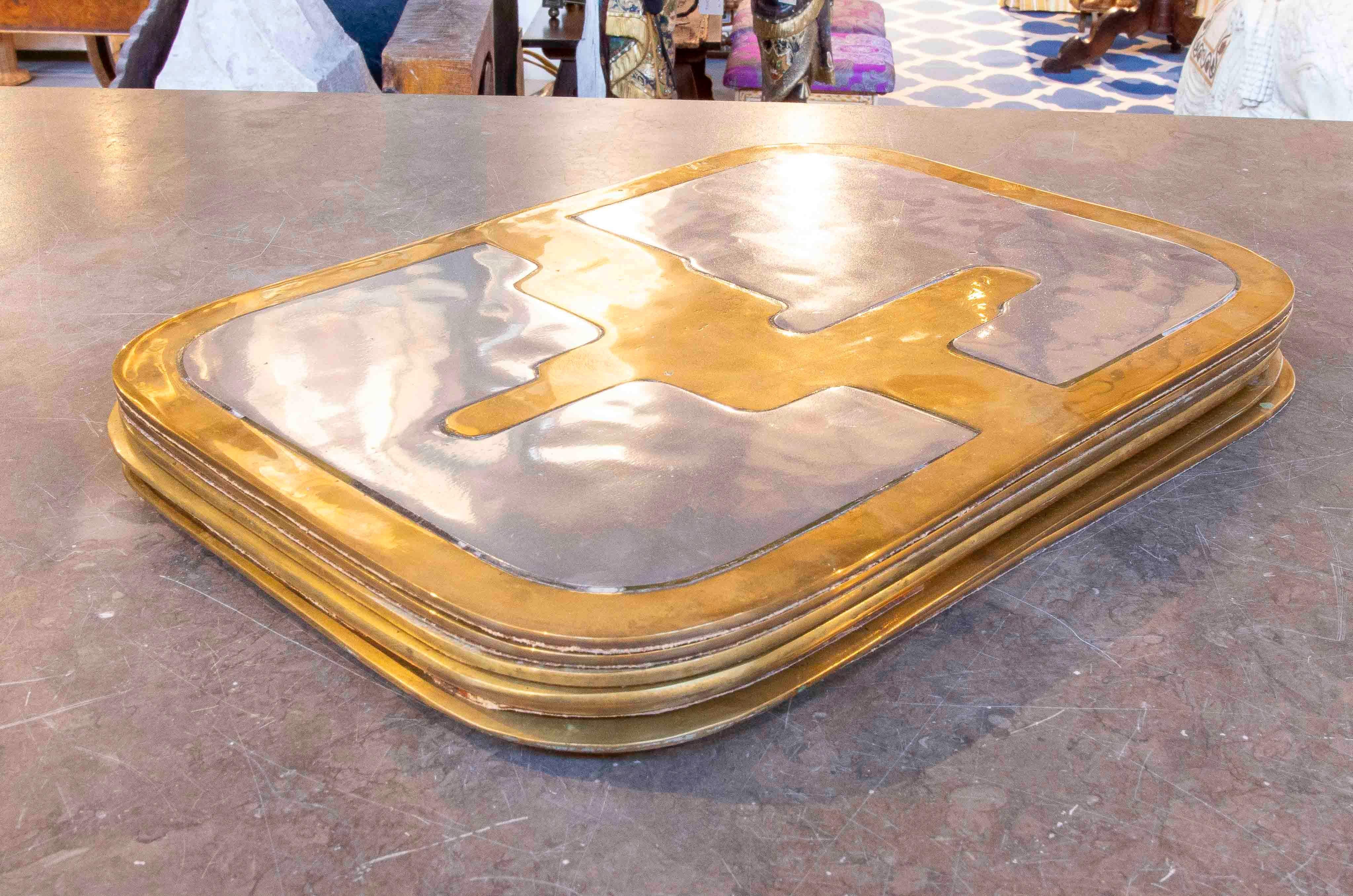 Ein elegantes Set aus sieben Tischsets, entworfen von David Marshall, hergestellt aus massivem Messing und Aluminium mit einem unverwechselbaren modernistischen geometrischen Design. Jedes Stück verbindet den warmen Glanz von Messing mit der