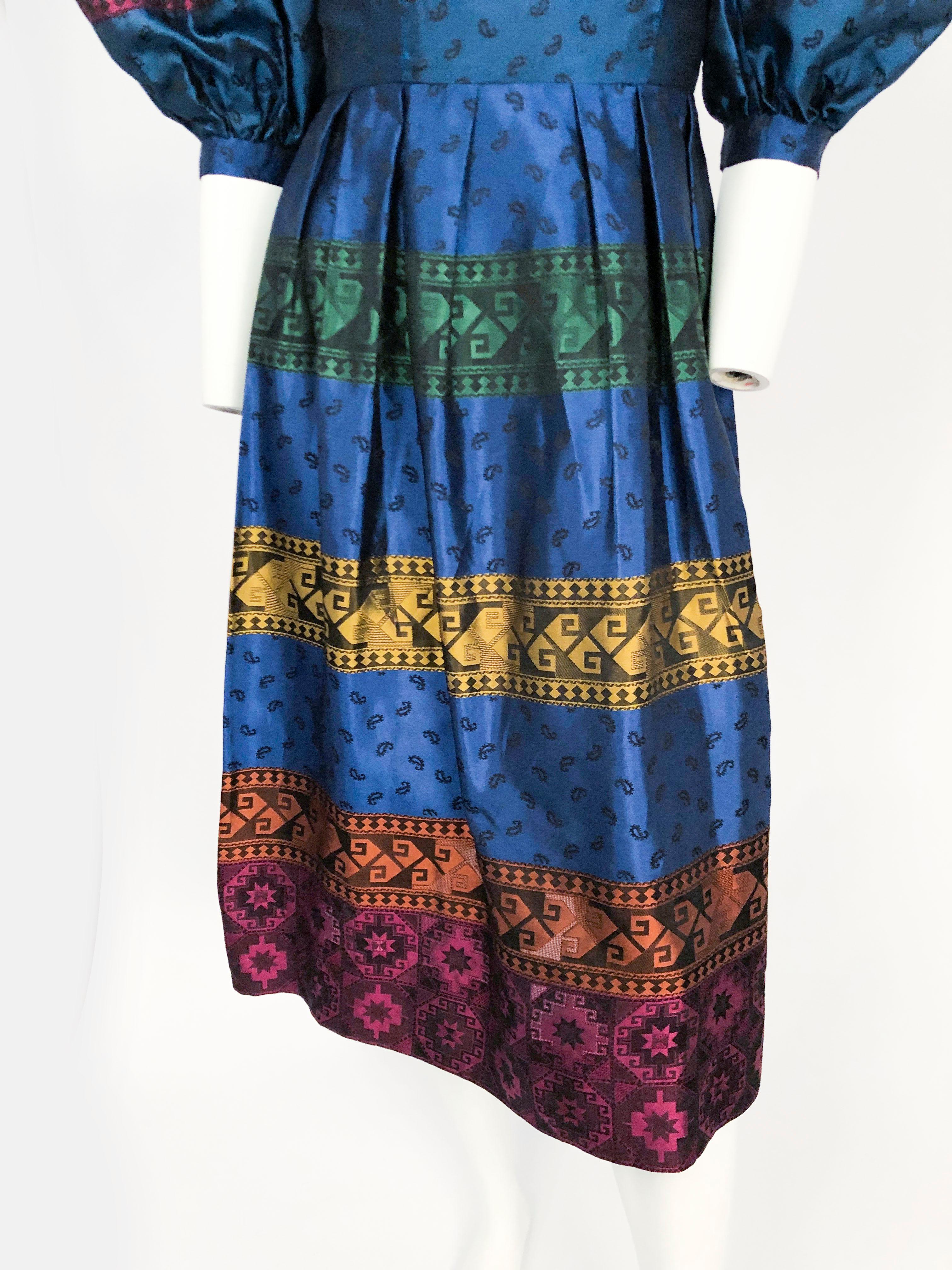 mehrfarbiges Kleid aus Seidenbrokat aus den 1980er Jahren mit übergroßen Puffärmeln, herzförmigem Ausschnitt, Bändern mit geometrischen Mustern und Pullwork. Die Ärmel sind ellbogenlang und mit einem 1-Zoll-Bündchen versehen.