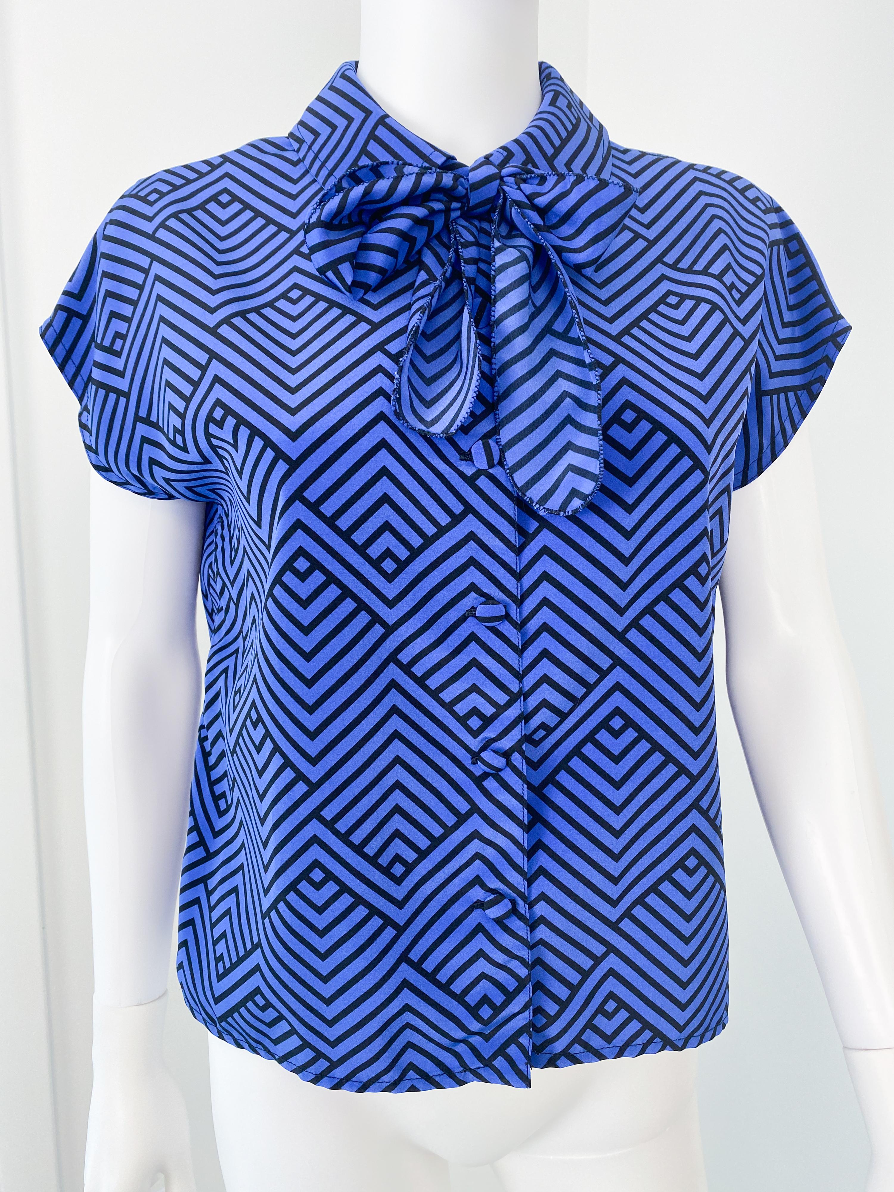 This stunning vintage 1980s blouse is made from silky viscose-polyester and features a classic pussy bow with its original tie. The fabric showcases a bold zig-zag pattern in electric blue and black, adding a striking touch. Designed with short